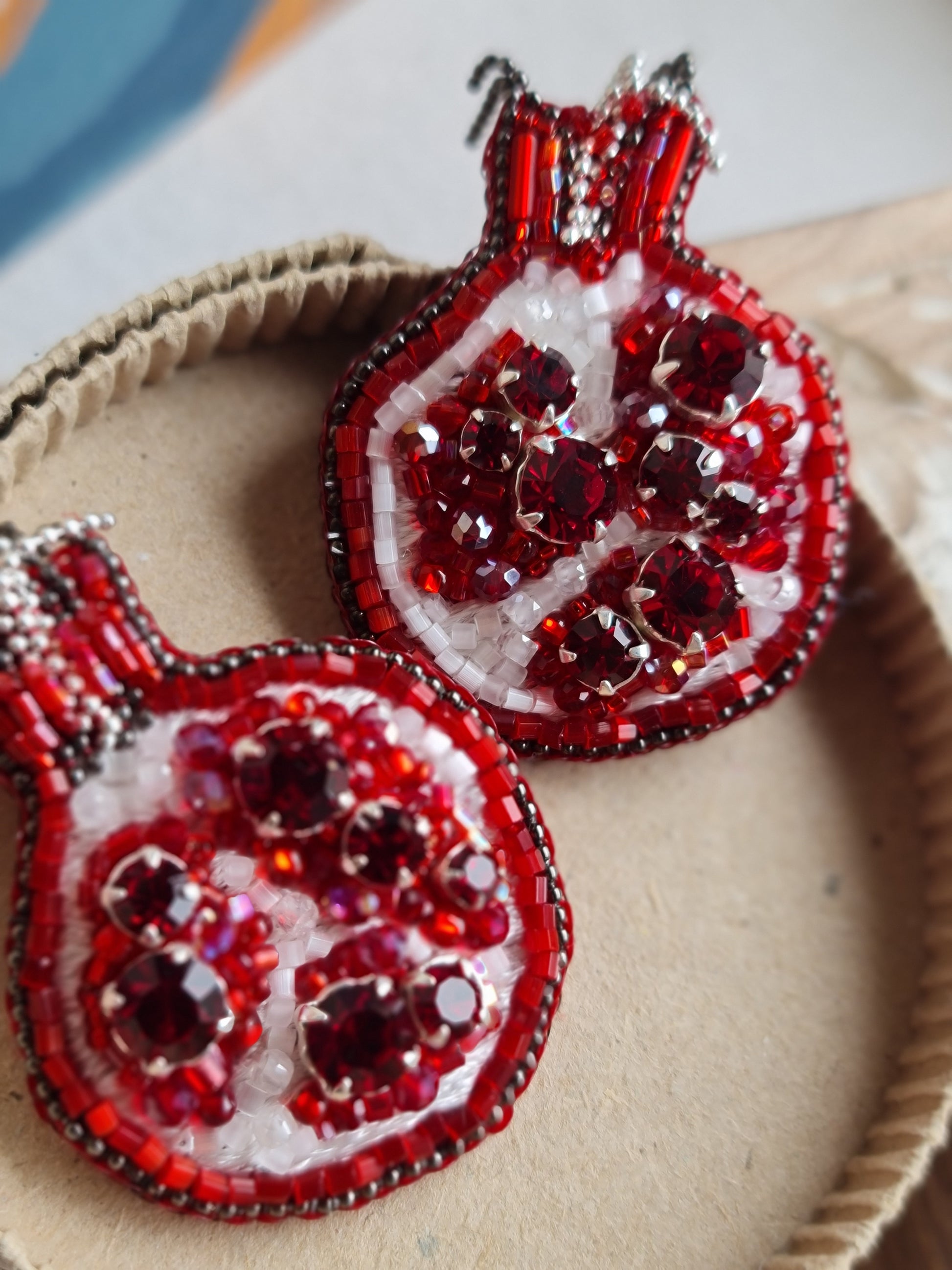 Red beaded pomegranate earrings on a textured surface