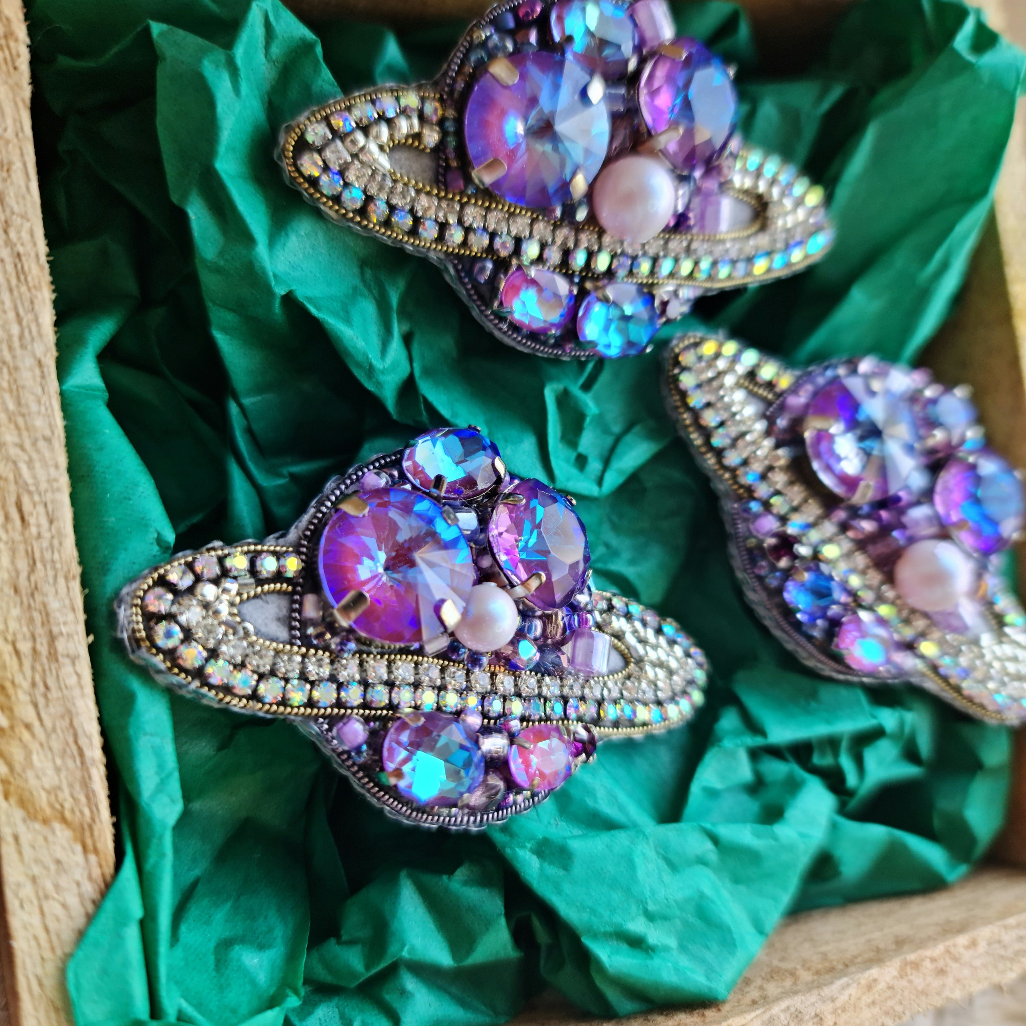 Decorative brooches with gemstones on green fabric inside a wooden box