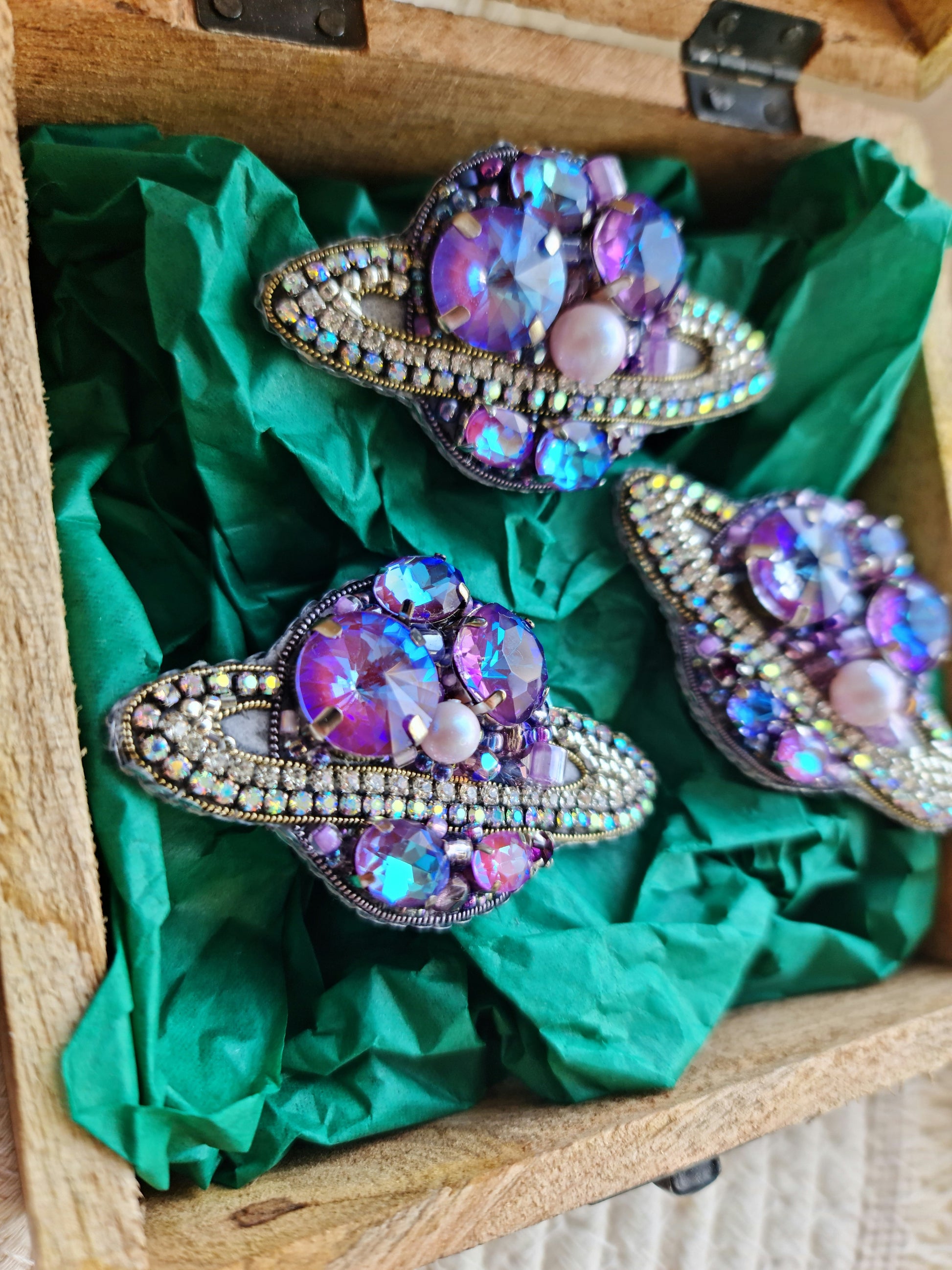 Decorative brooches with gemstones on green fabric inside a wooden box