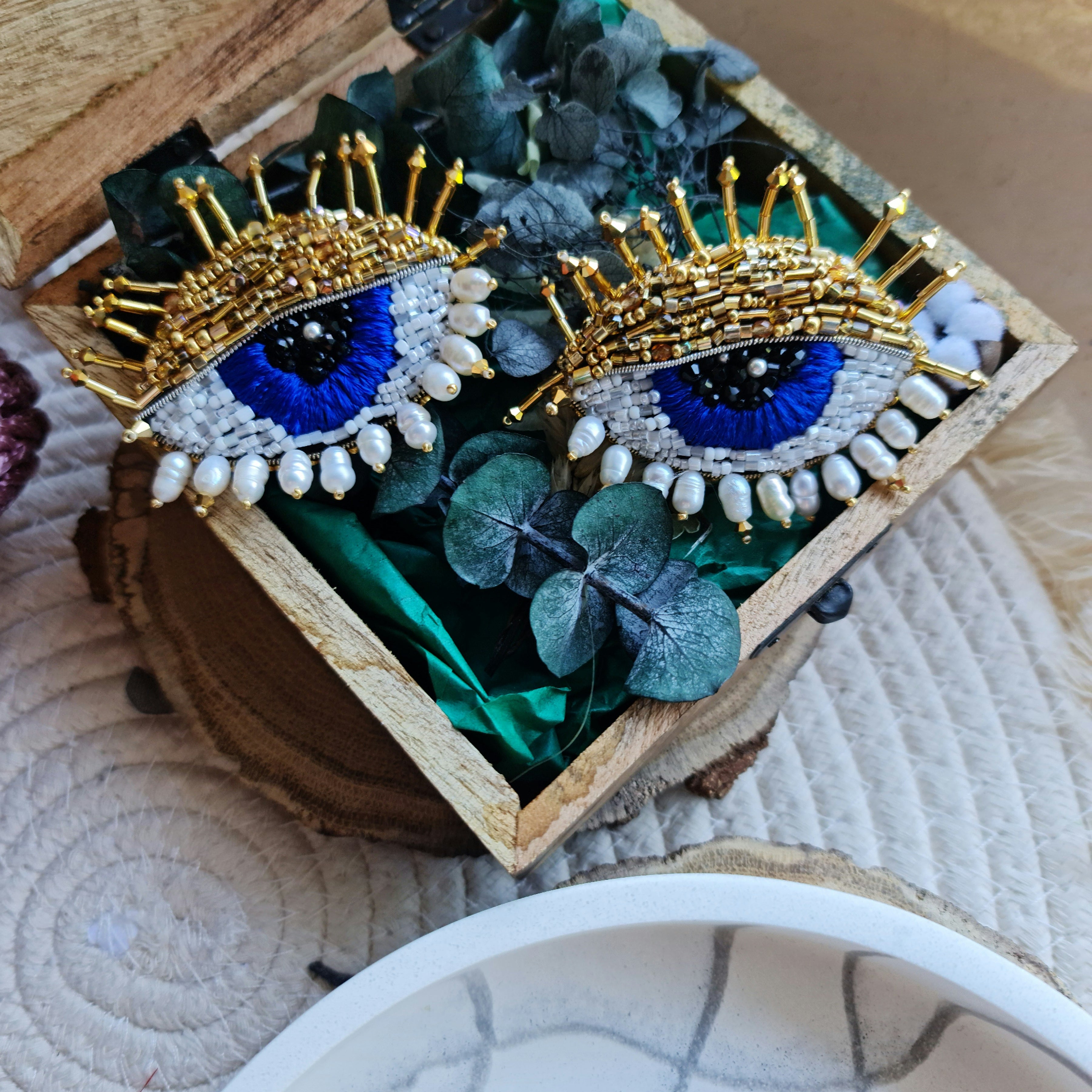 Close-up view of the intricate beadwork on the blue eye brooch, showcasing shimmering glass beads, crystals, and plastic beads fixed onto felt