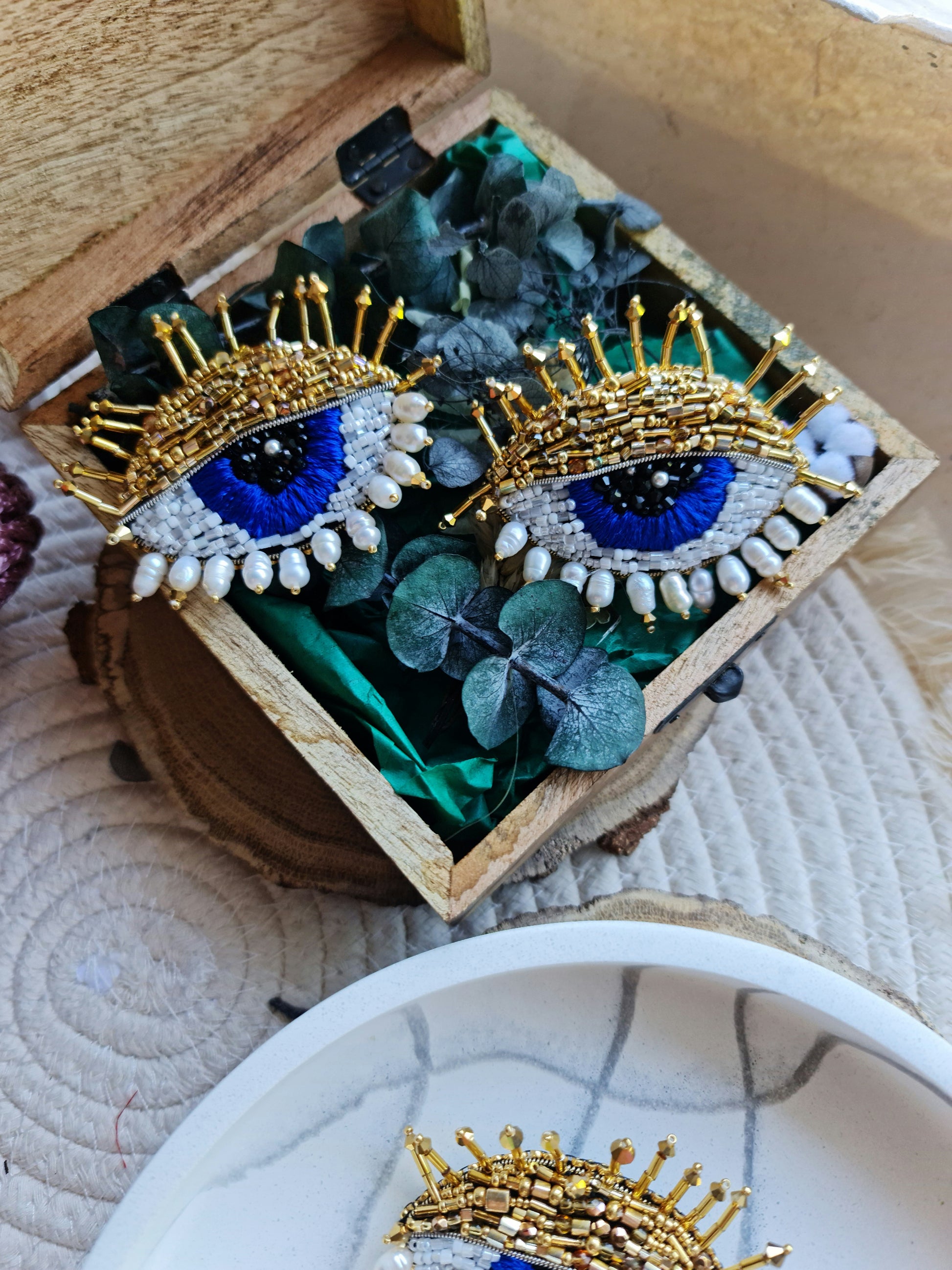 Close-up view of the intricate beadwork on the blue eye brooch, showcasing shimmering glass beads, crystals, and plastic beads fixed onto felt