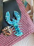 Close-up view of the intricate beadwork and secure fastening on a handmade lobster brooch, highlighting its vibrant red/blue color and ocean-inspired design