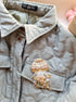 Close-up of a quilted jacket with a decorative brooch on a neutral background