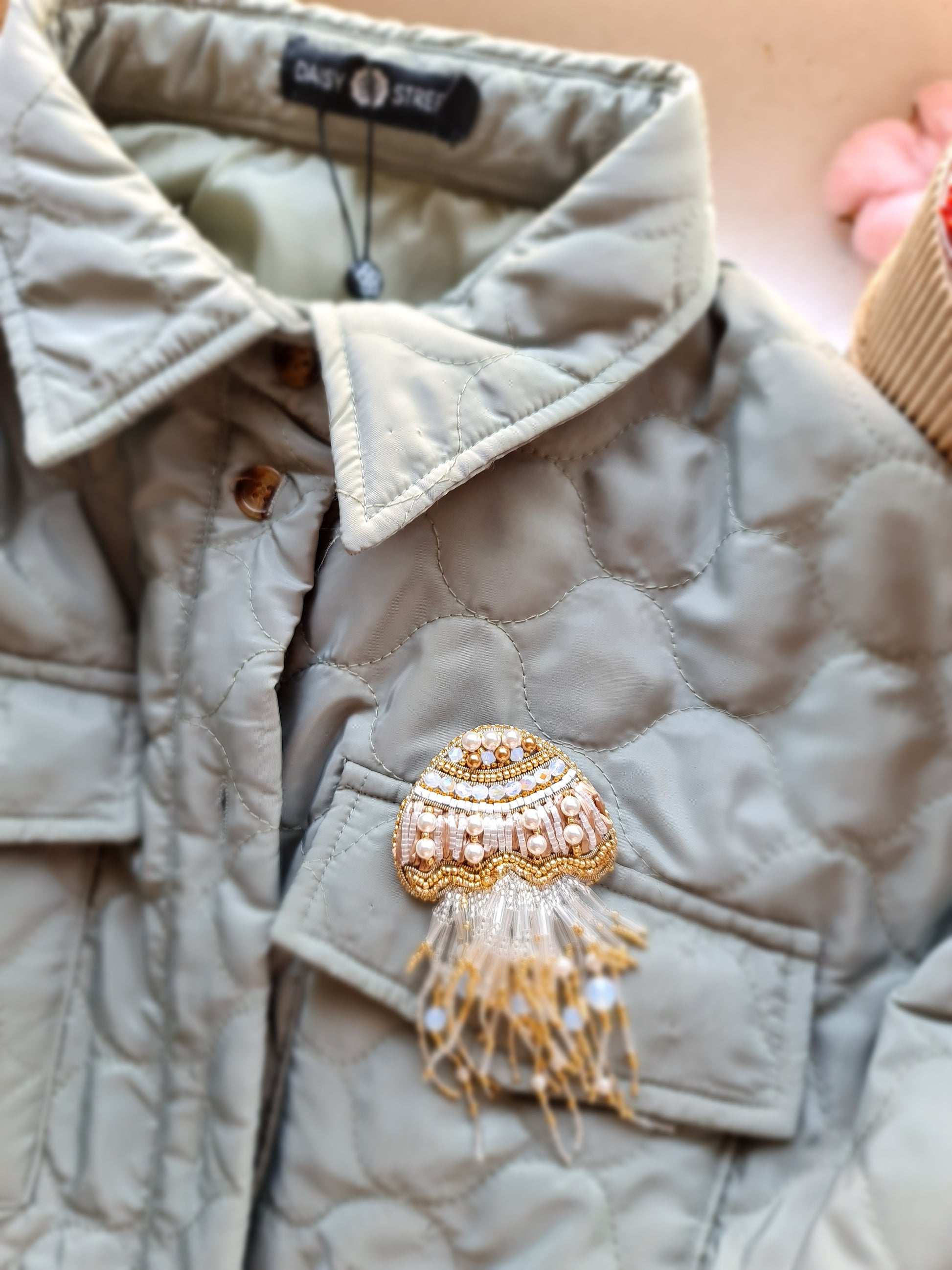 Close-up of a quilted jacket with a decorative brooch on a neutral background