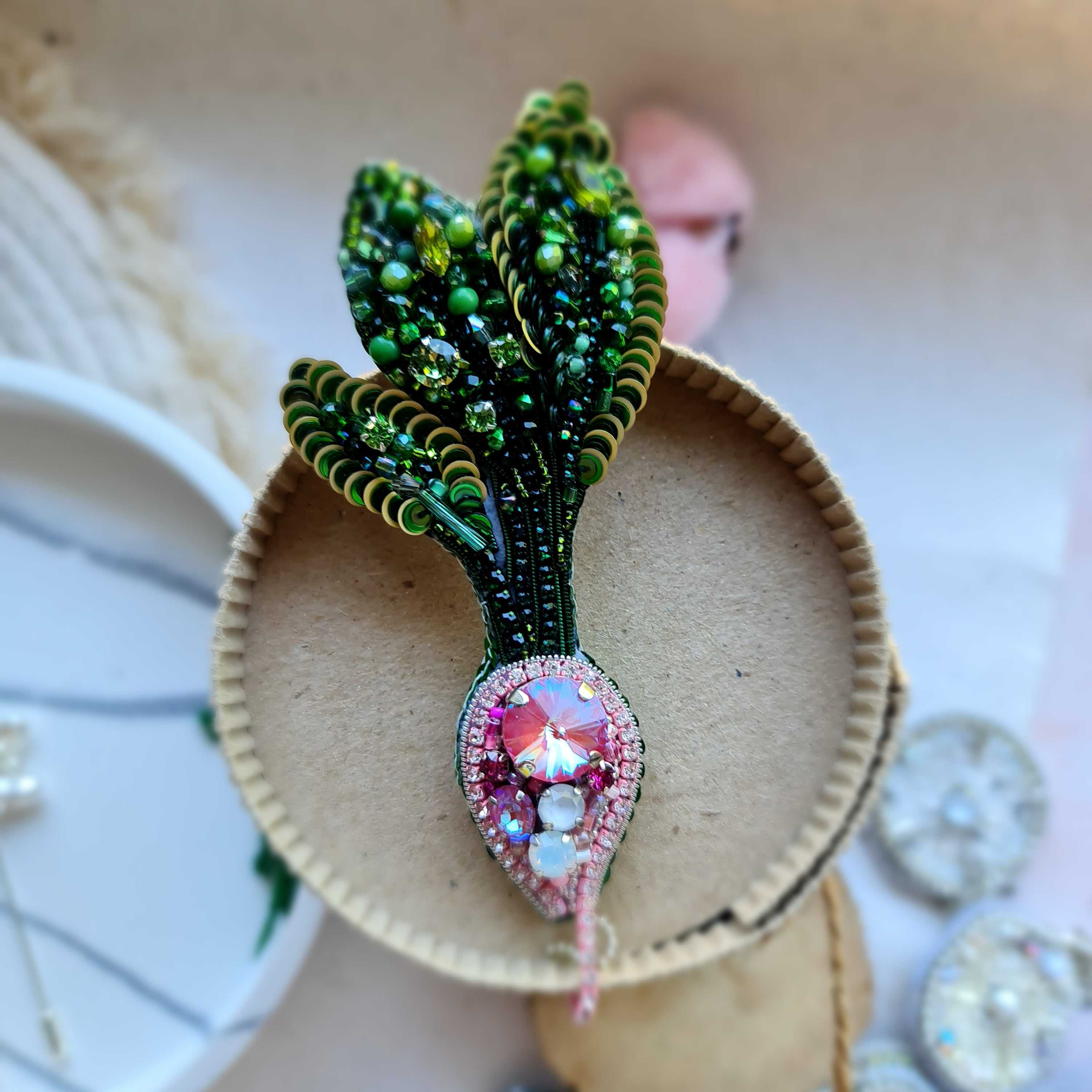 Handmade radish beaded brooch with green leaves, a pink crystal center, and sparkling embroidered details