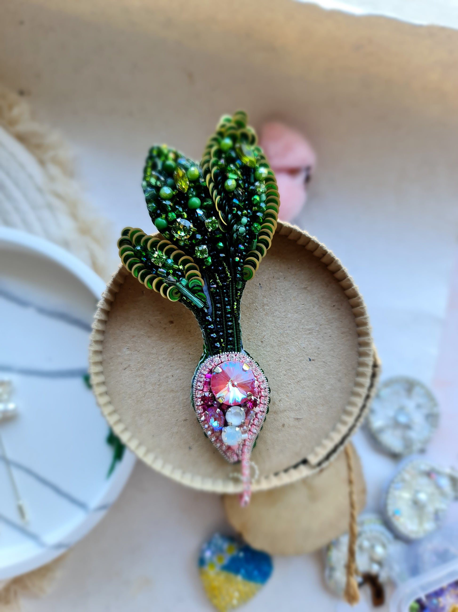 Handmade radish beaded brooch with green leaves, a pink crystal center, and sparkling embroidered details