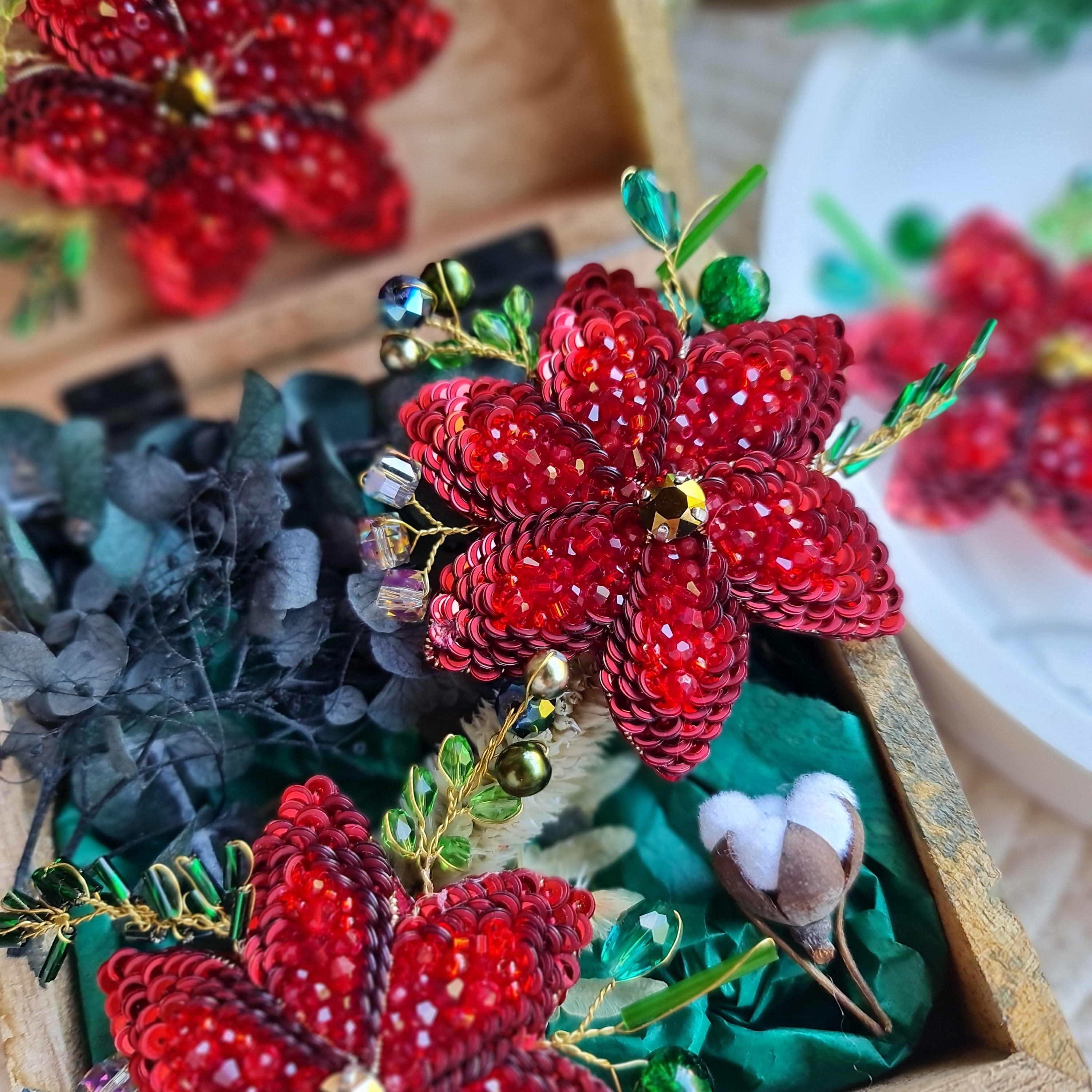 Decorative red flower brooch with green leaves in a wooden box.