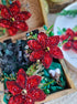 Decorative red flower brooch with green leaves in a wooden box.