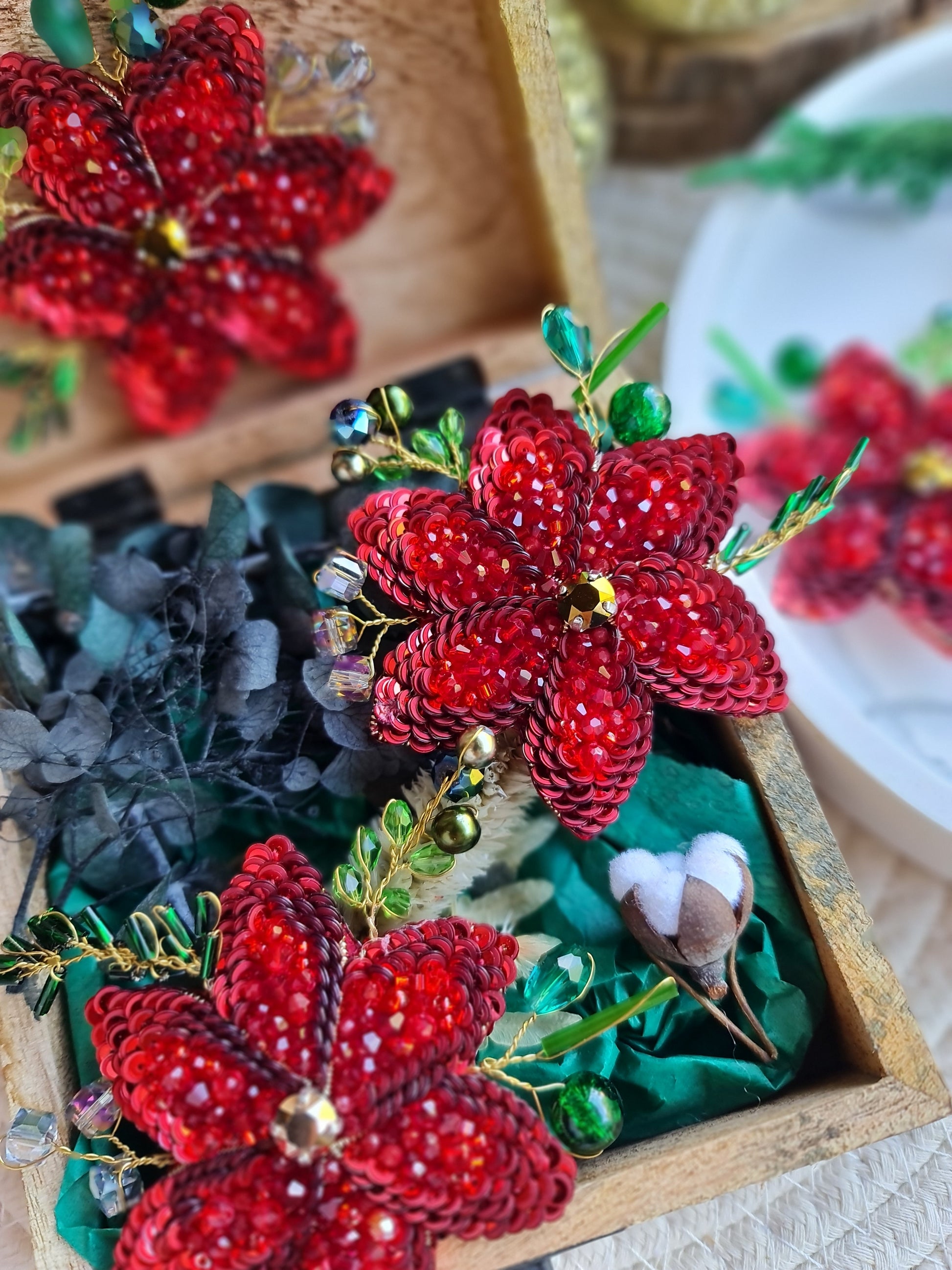 Decorative red flower brooch with green leaves in a wooden box.