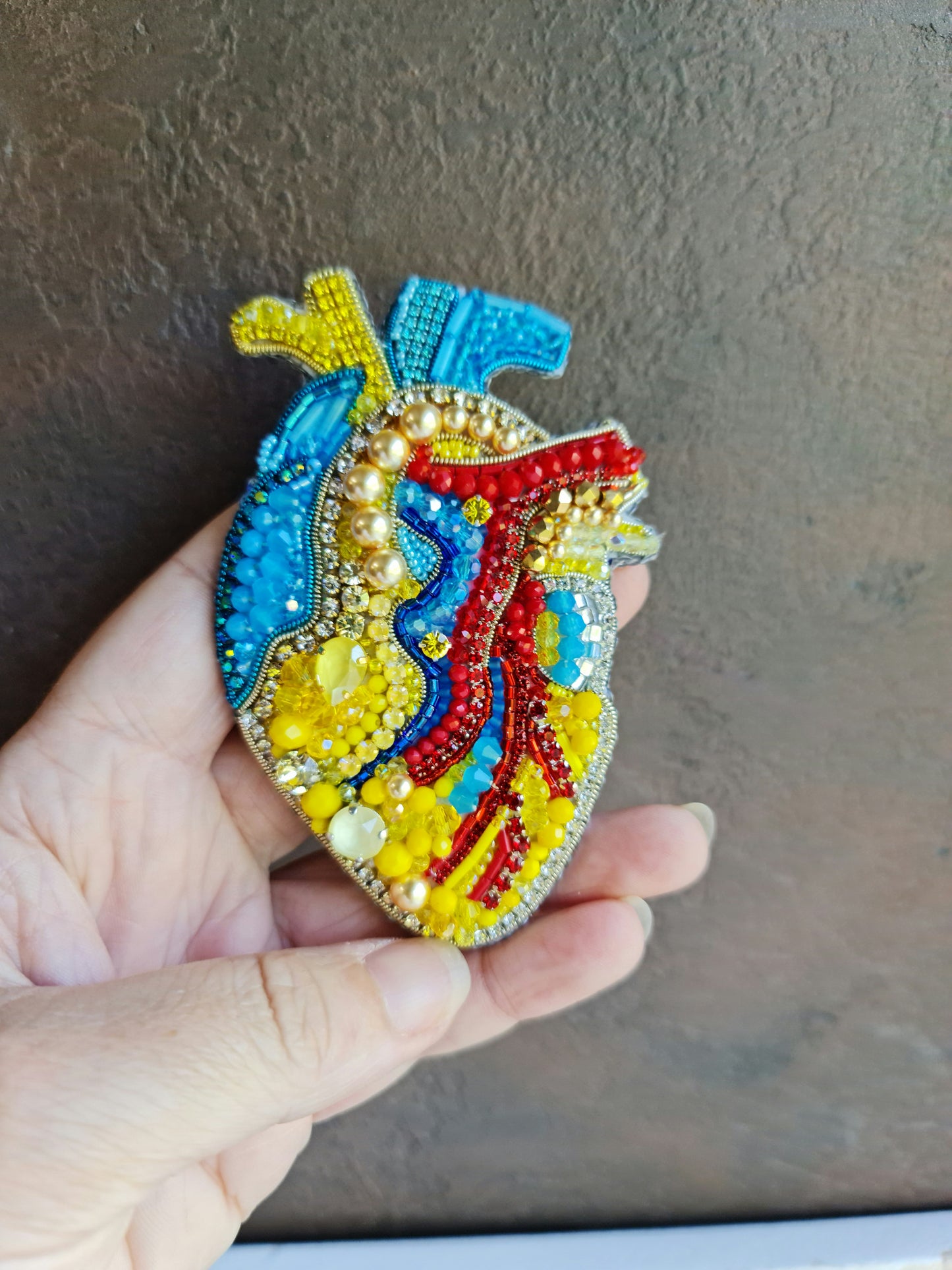 Close-up of the anatomical heart brooch showing detailed stitching and vibrant embroidered patterns.