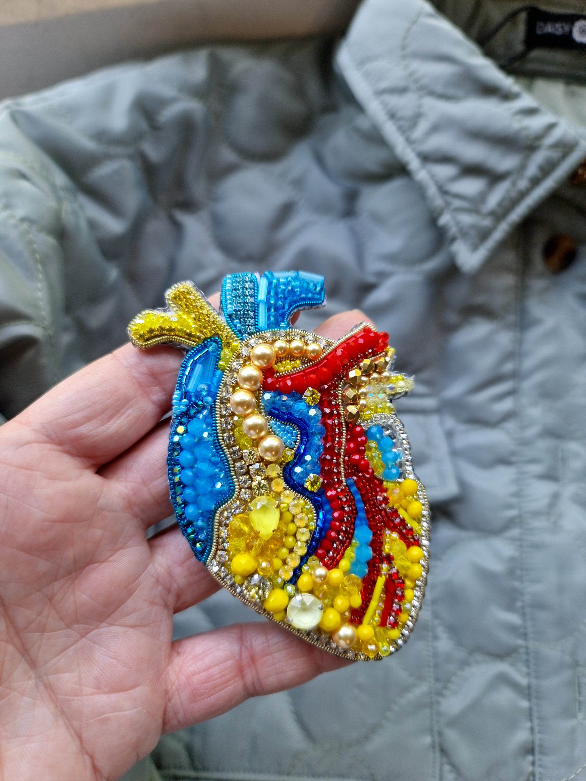 Close-up of the anatomical heart brooch showing detailed stitching and vibrant embroidered patterns.