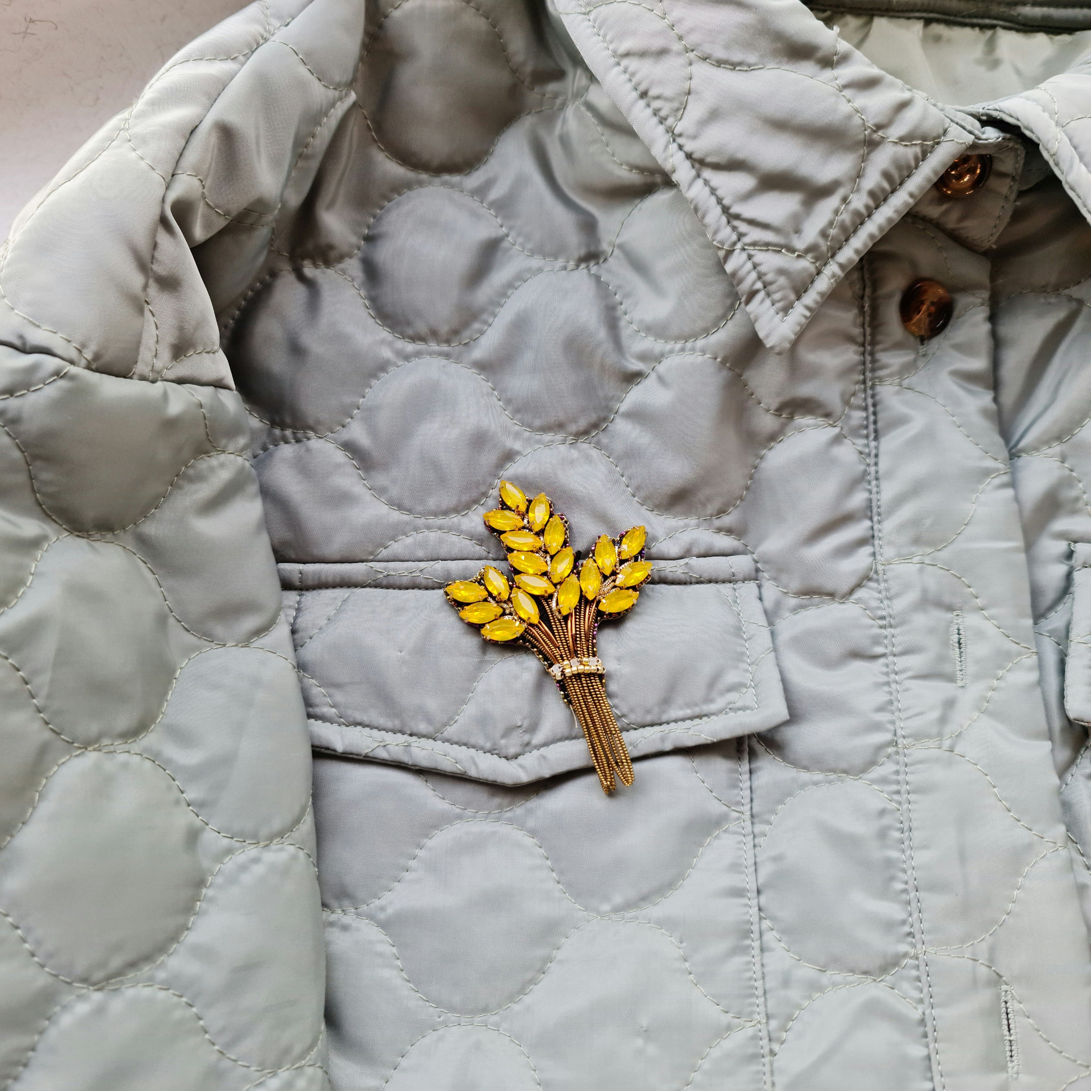 Light gray quilted jacket with a brooch featuring yellow flowers on a matching background