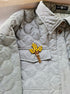 Light gray quilted jacket with a brooch featuring yellow flowers on a matching background