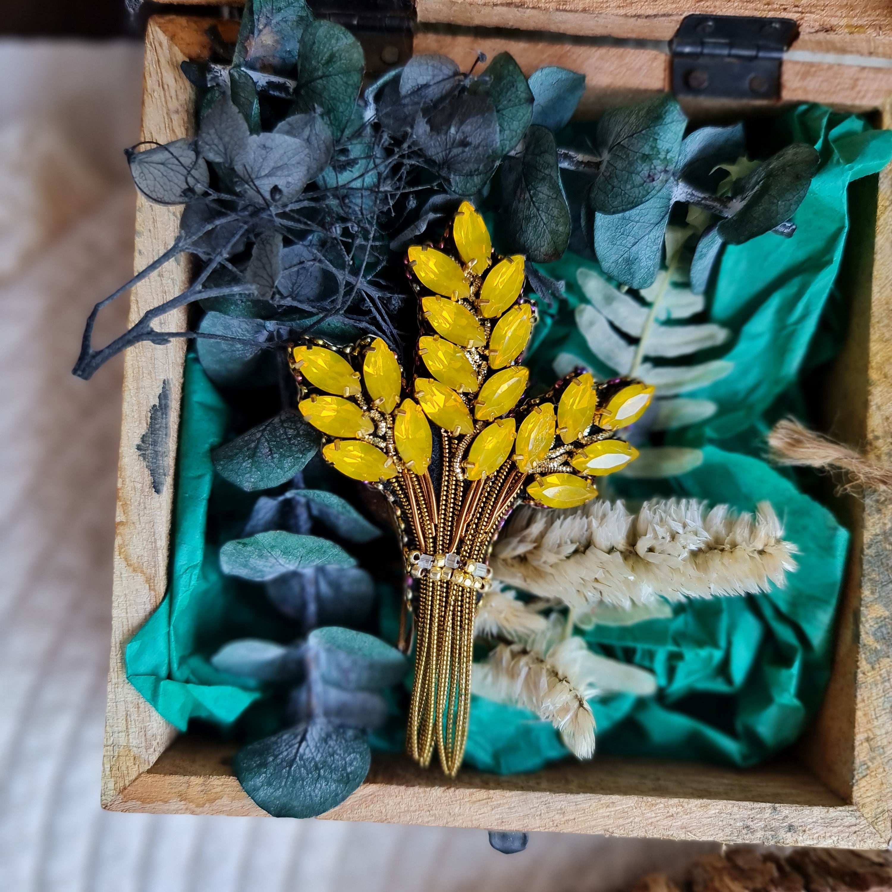 Decorative brooch with yellow flowers and green leaves in a wooden box.