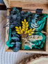 Decorative brooch with yellow flowers and green leaves in a wooden box.