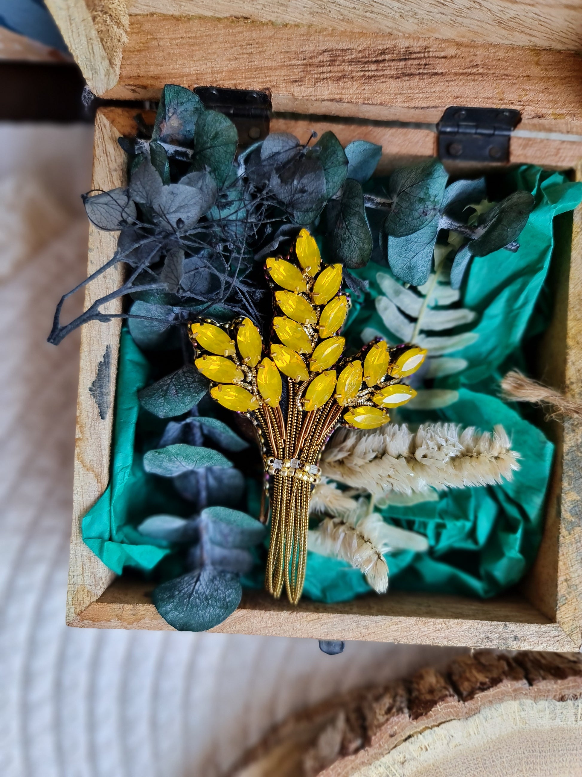 Decorative brooch with yellow flowers and green leaves in a wooden box.