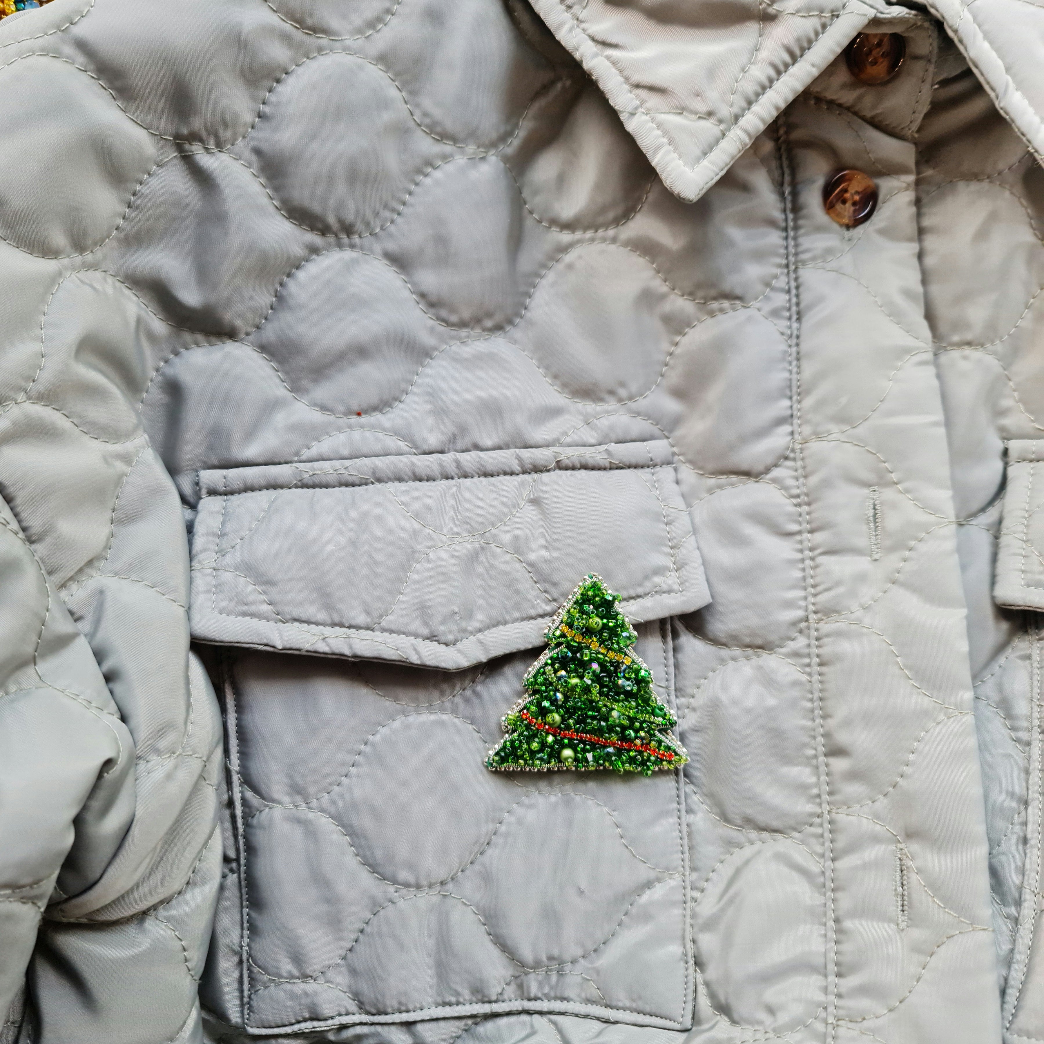 Quilted jacket with a Christmas tree patch on a neutral background