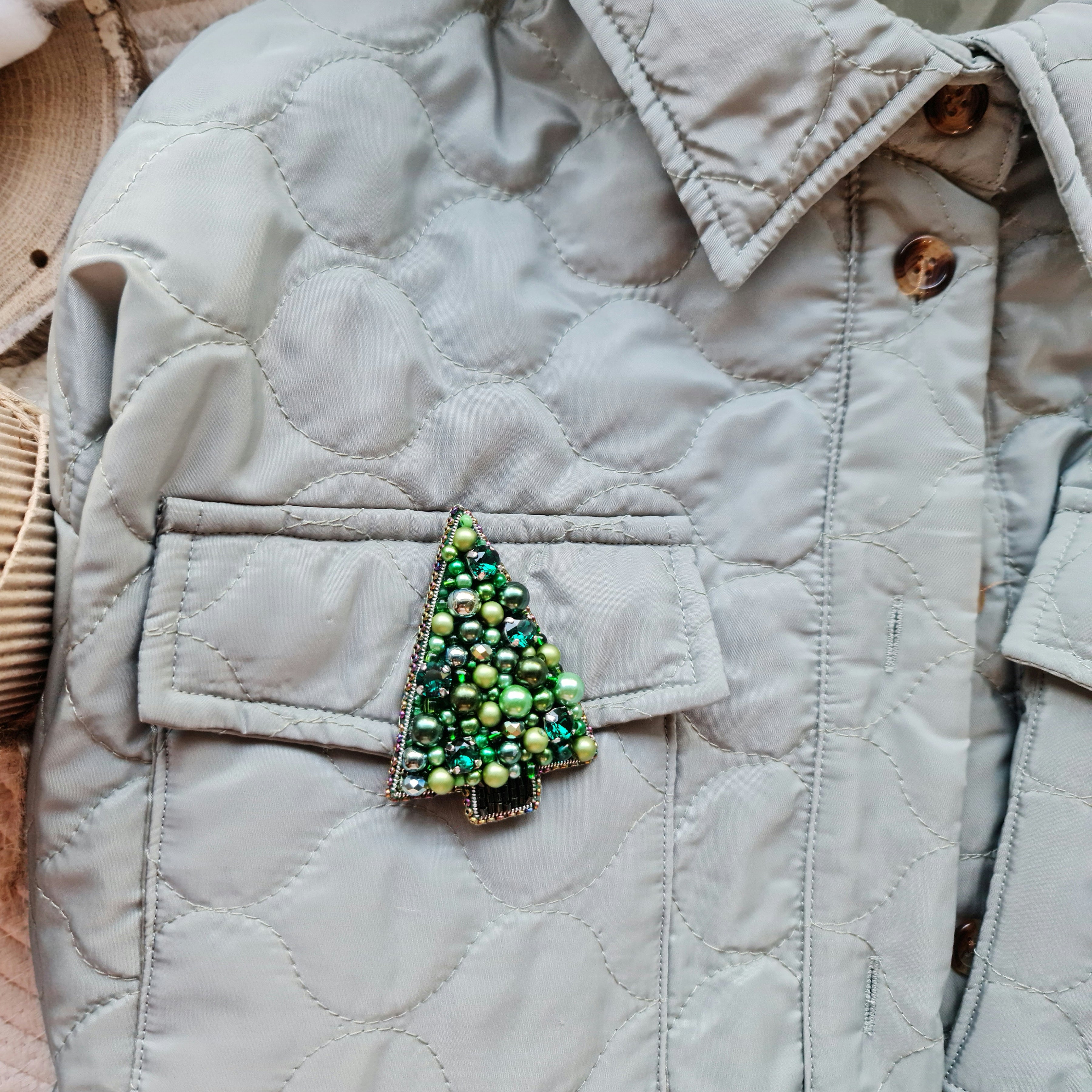 Quilted jacket with a decorative green tree brooch on a neutral background