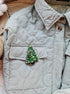 Quilted jacket with a decorative green tree brooch on a neutral background