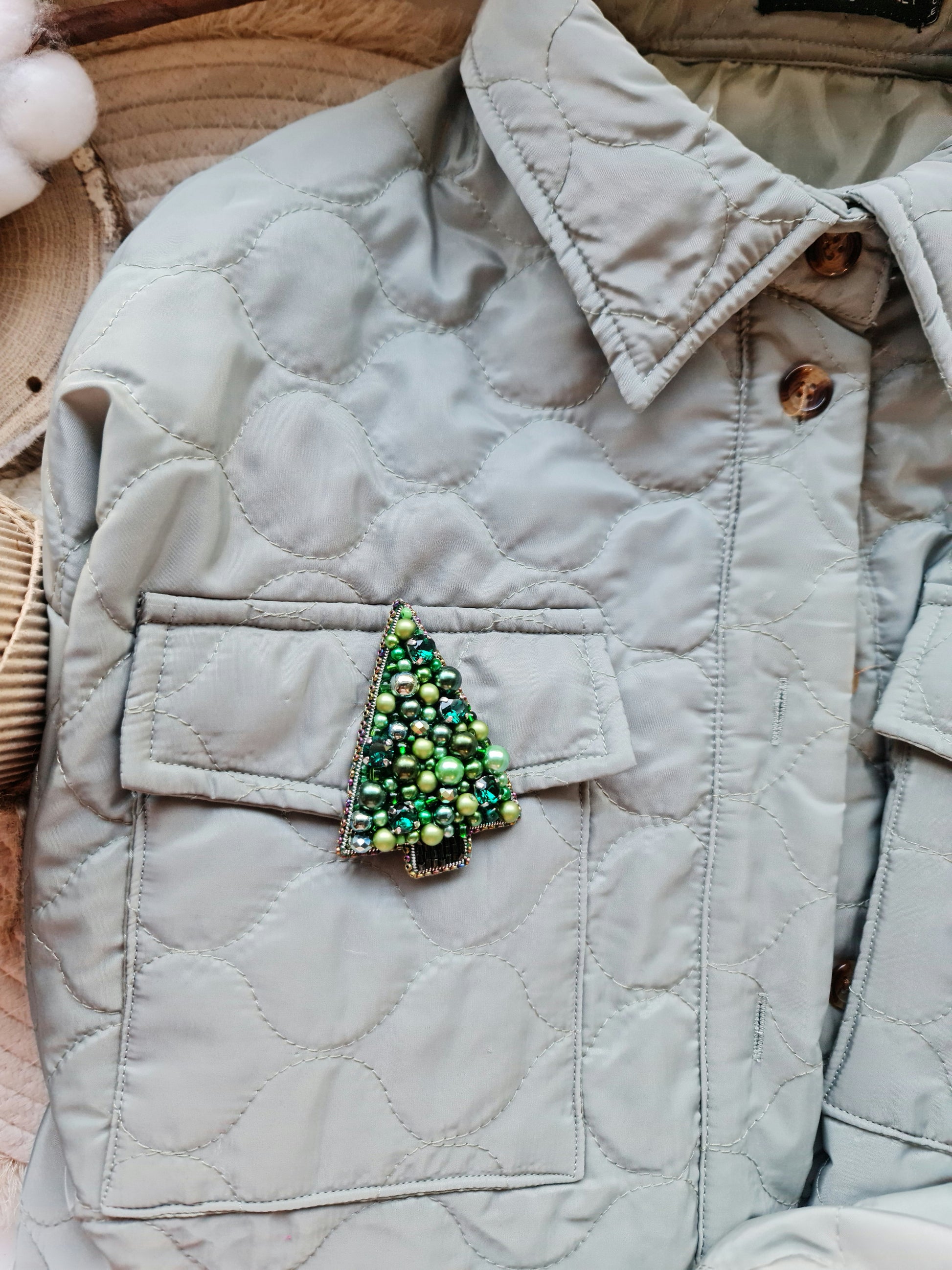 Quilted jacket with a decorative green tree brooch on a neutral background