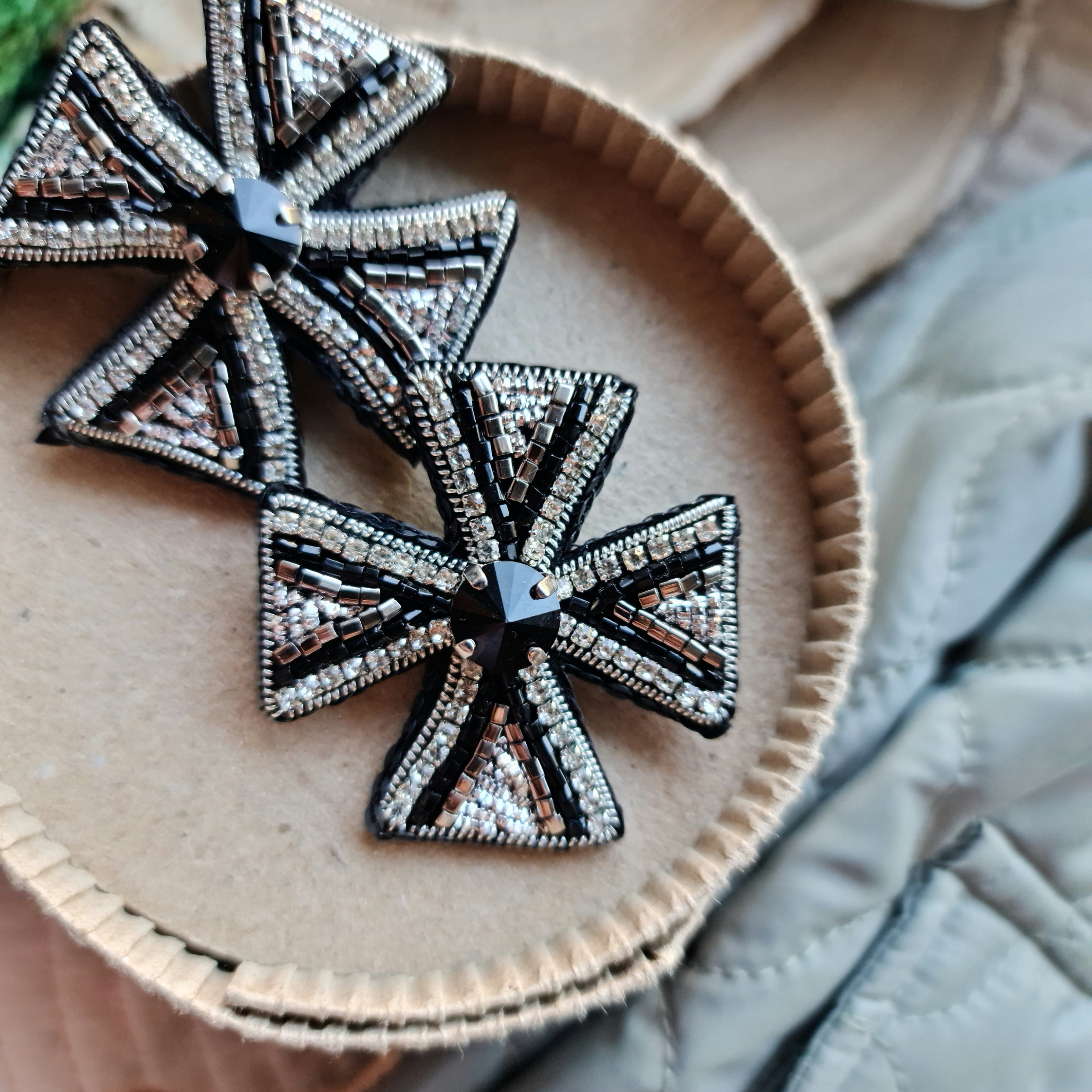 Decorative cross-shaped brooches on a wooden surface with a natural background.