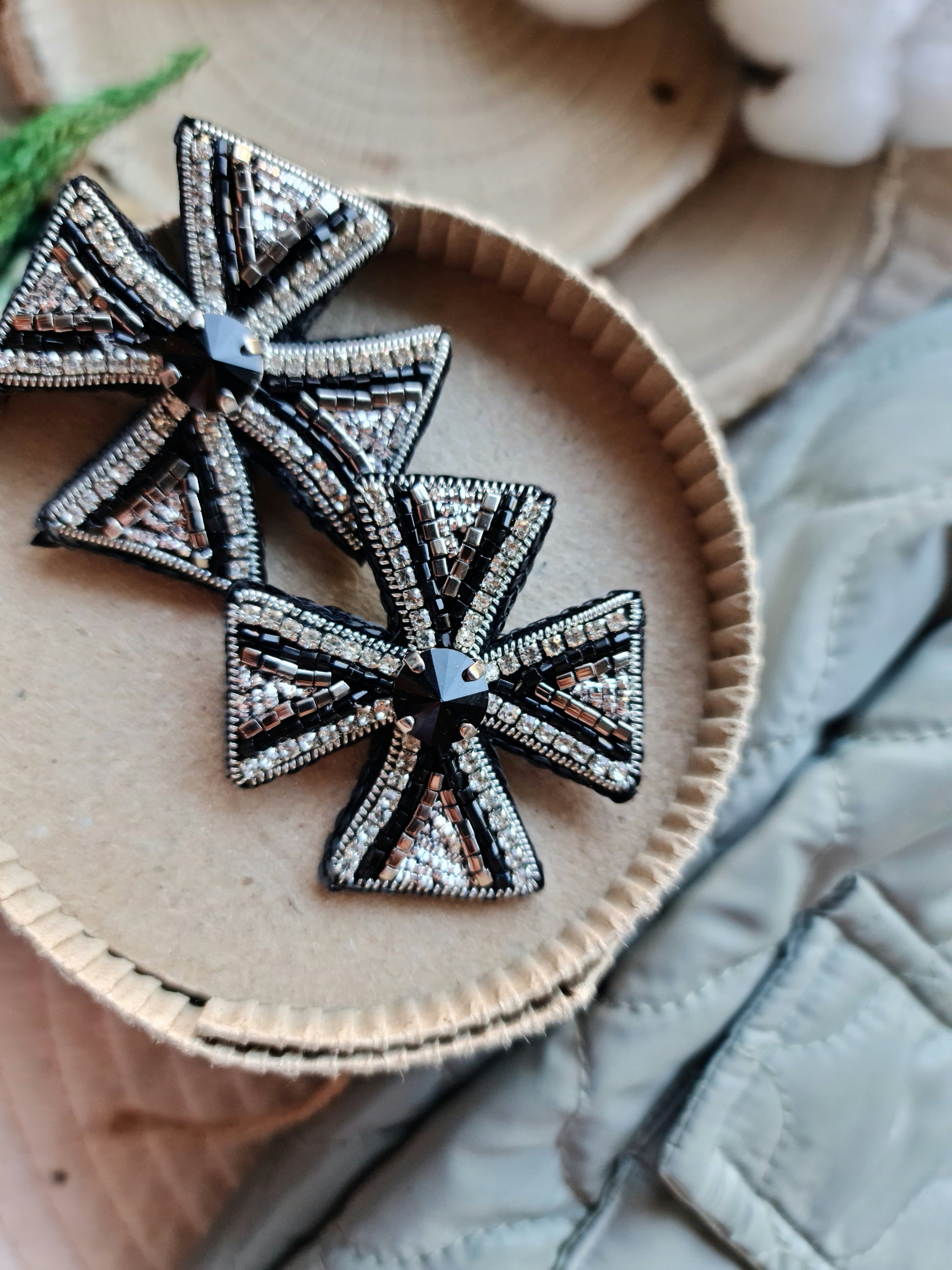 Decorative cross-shaped brooches on a wooden surface with a natural background.