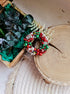 Decorative wreath with red, green, and white beads on a wooden surface with greenery.