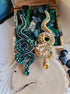 Two decorative snake-shaped pins, one green and one gold, on a wooden surface with greenery.