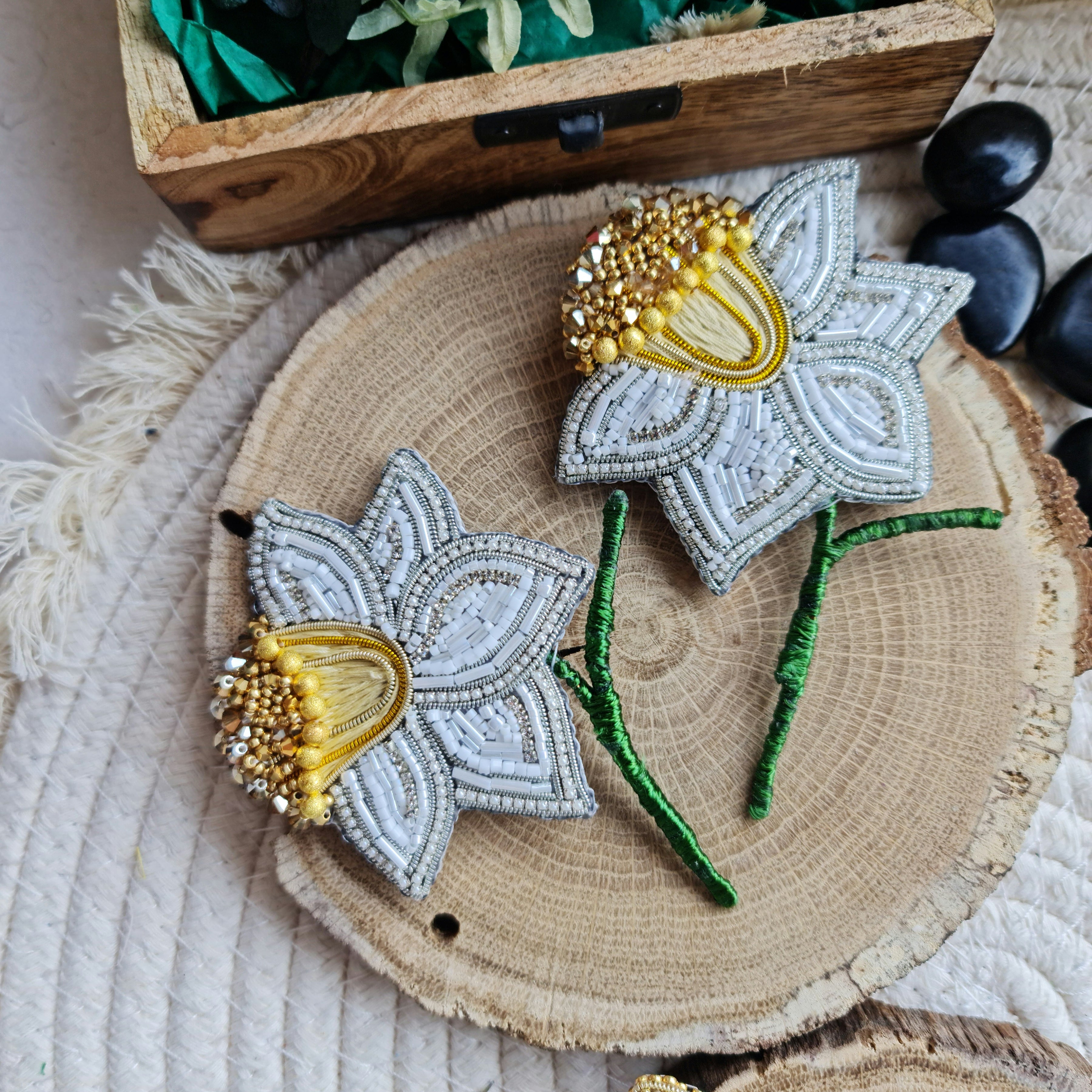 Decorative flower brooches on a wooden surface with a wooden box and stones in the background.