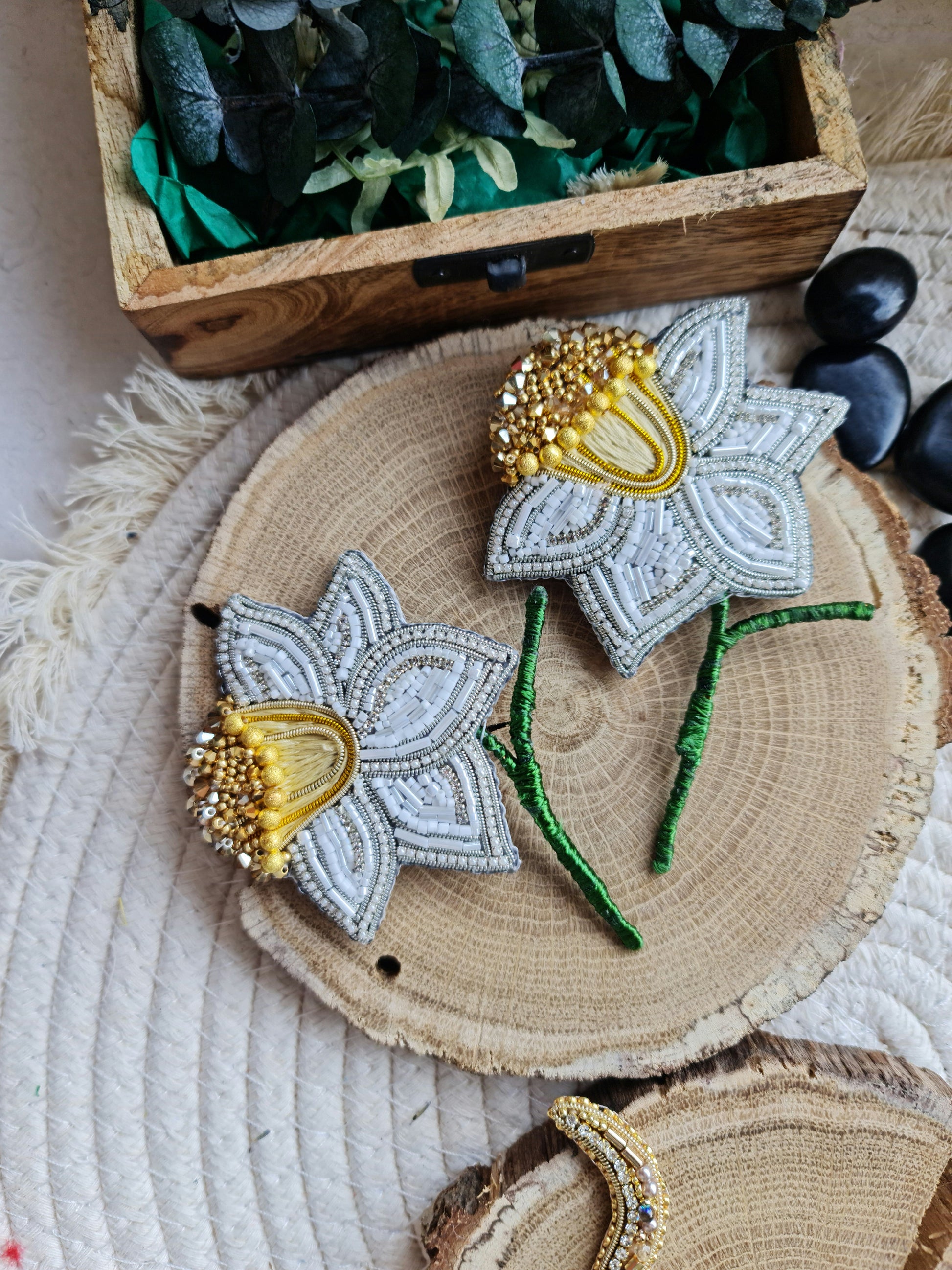 Decorative flower brooches on a wooden surface with a wooden box and stones in the background.