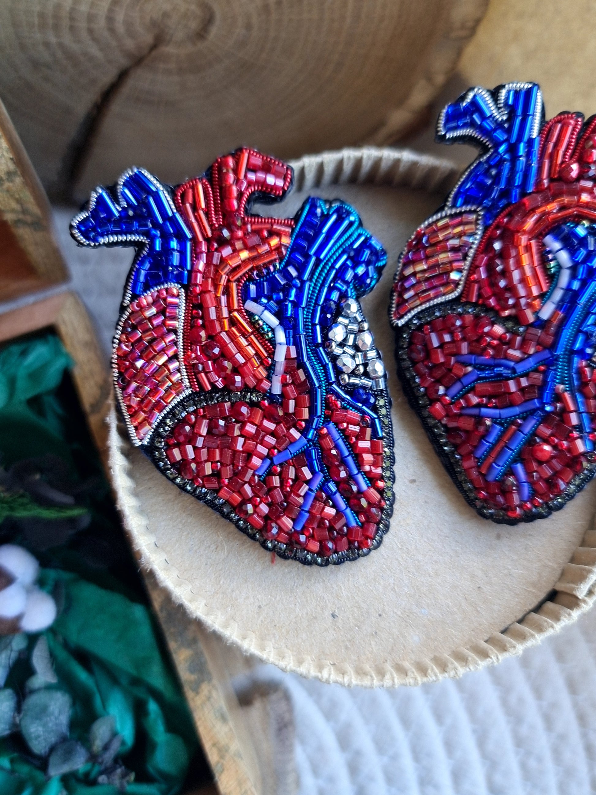 Two beaded heart-shaped brooches on a wooden surface