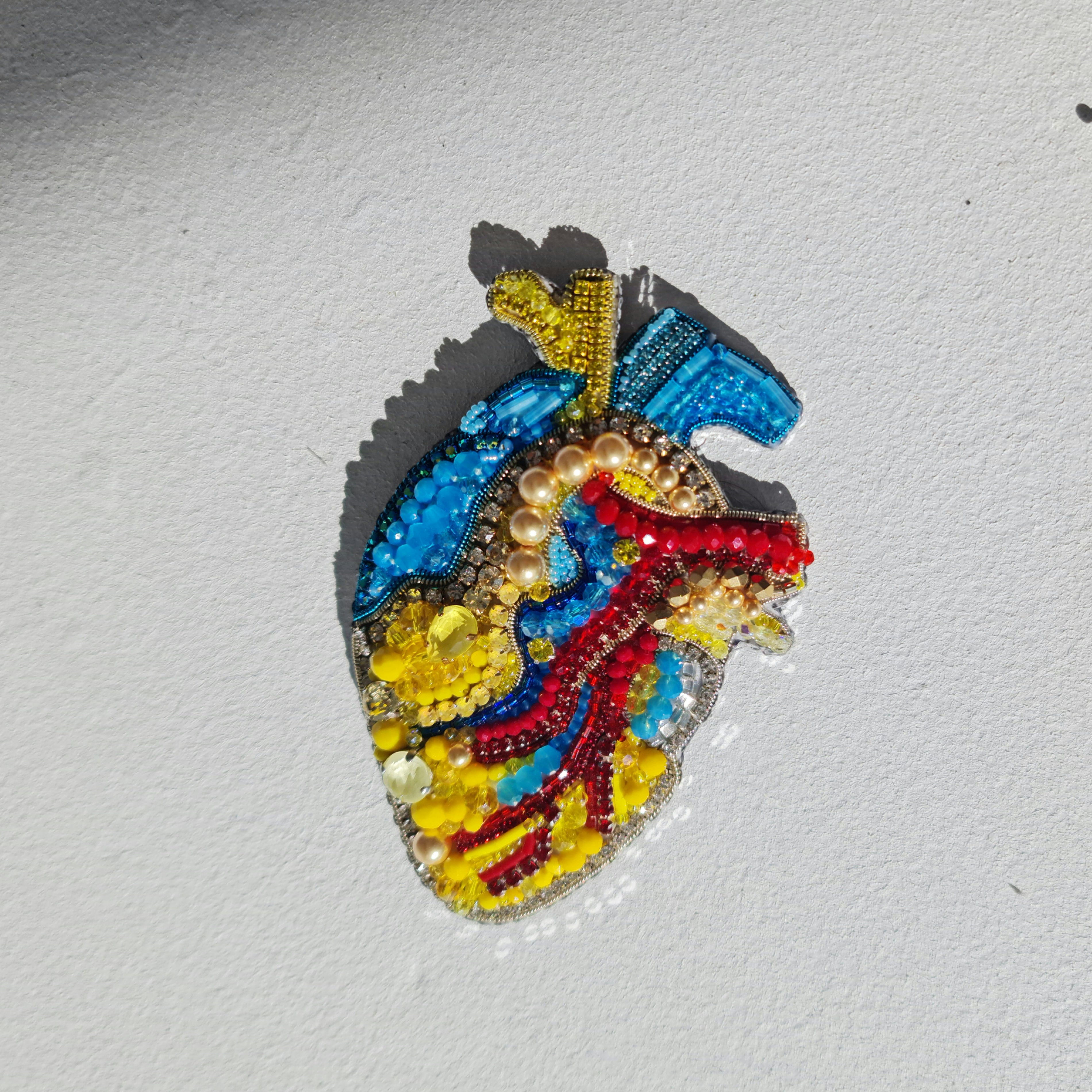 Close-up of the anatomical heart brooch showing detailed stitching and vibrant embroidered patterns.