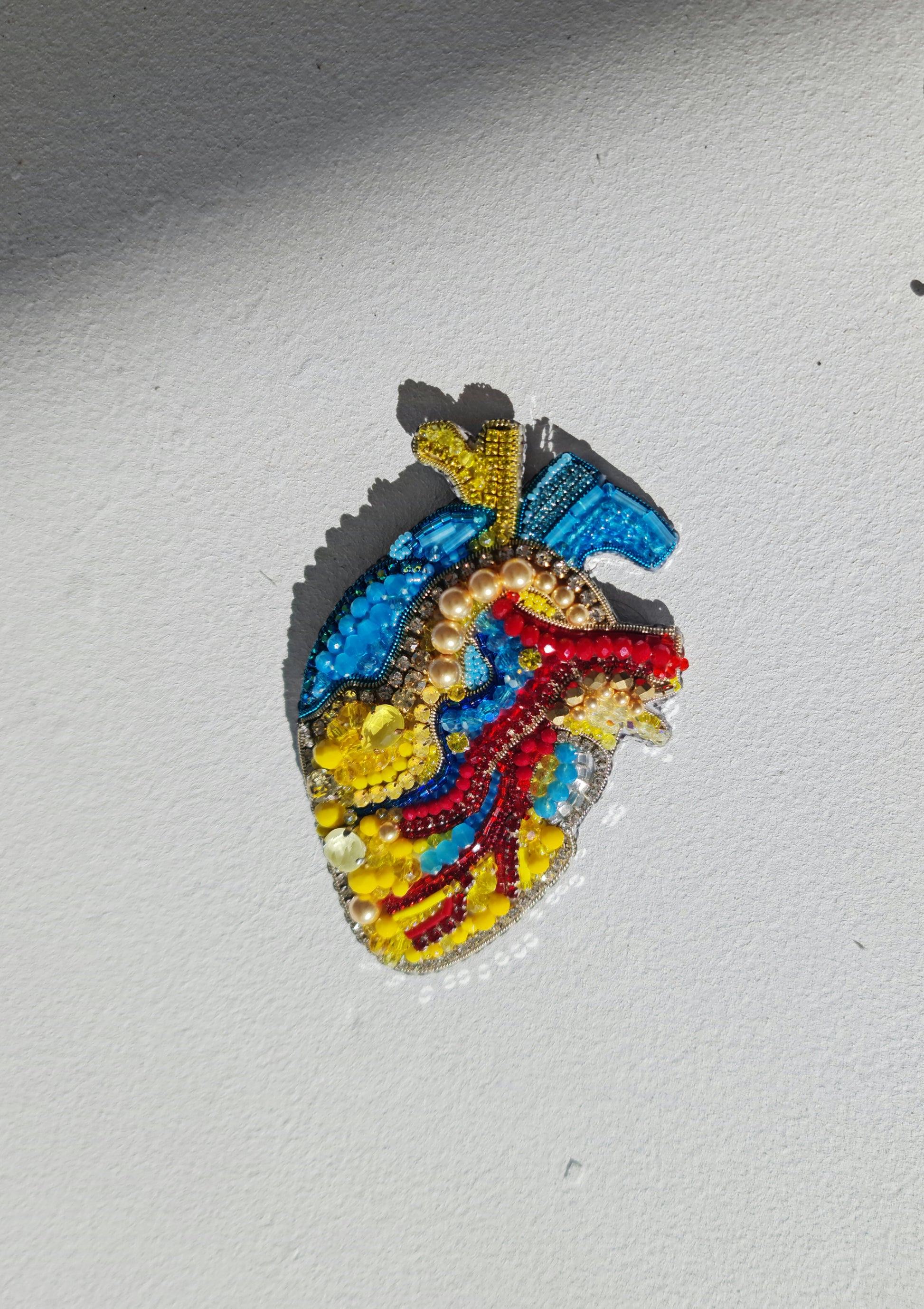 Close-up of the anatomical heart brooch showing detailed stitching and vibrant embroidered patterns.