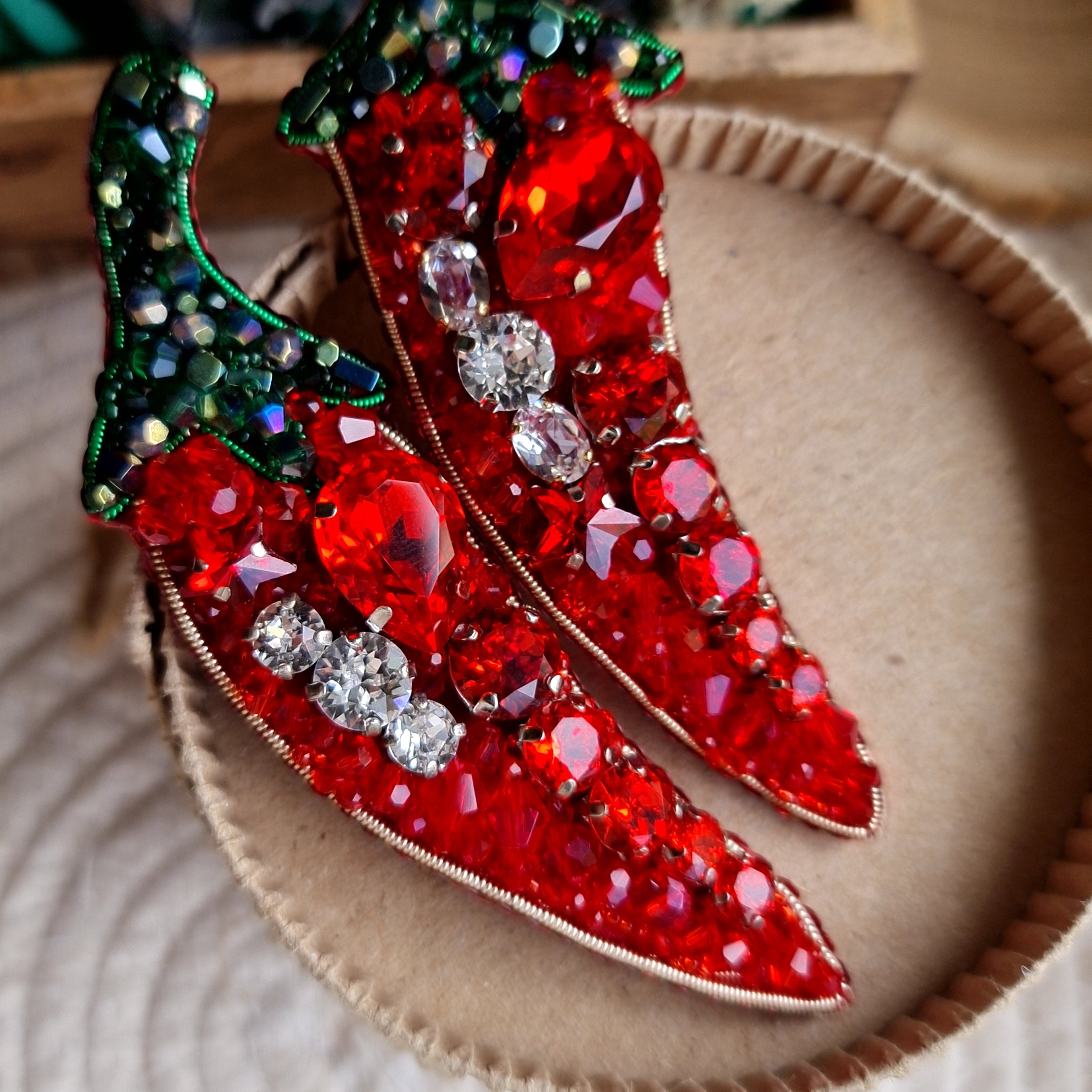 Decorative red chili pepper brooch with gemstones on a textured surface
