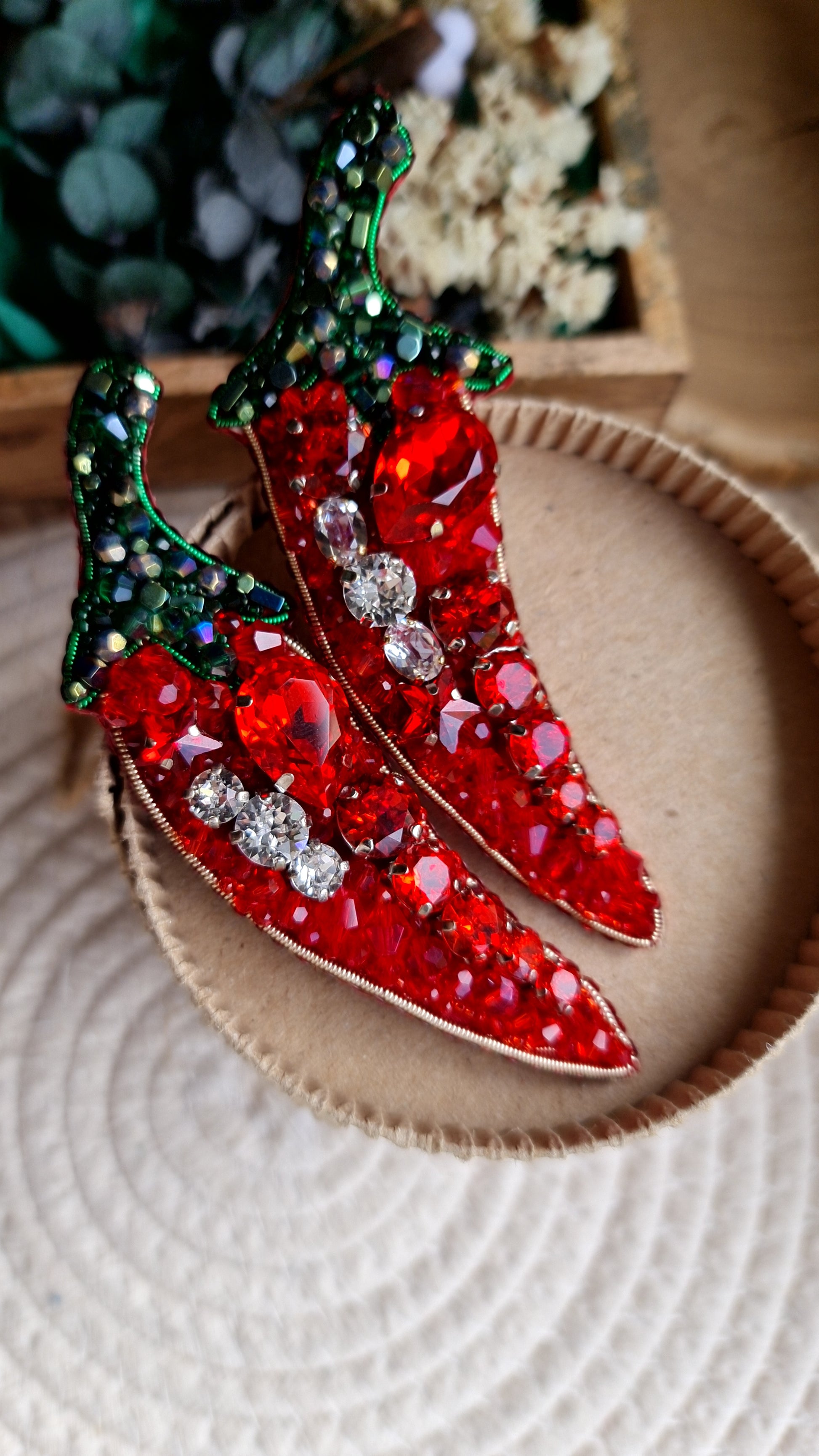 Decorative red chili pepper brooch with gemstones on a textured surface
