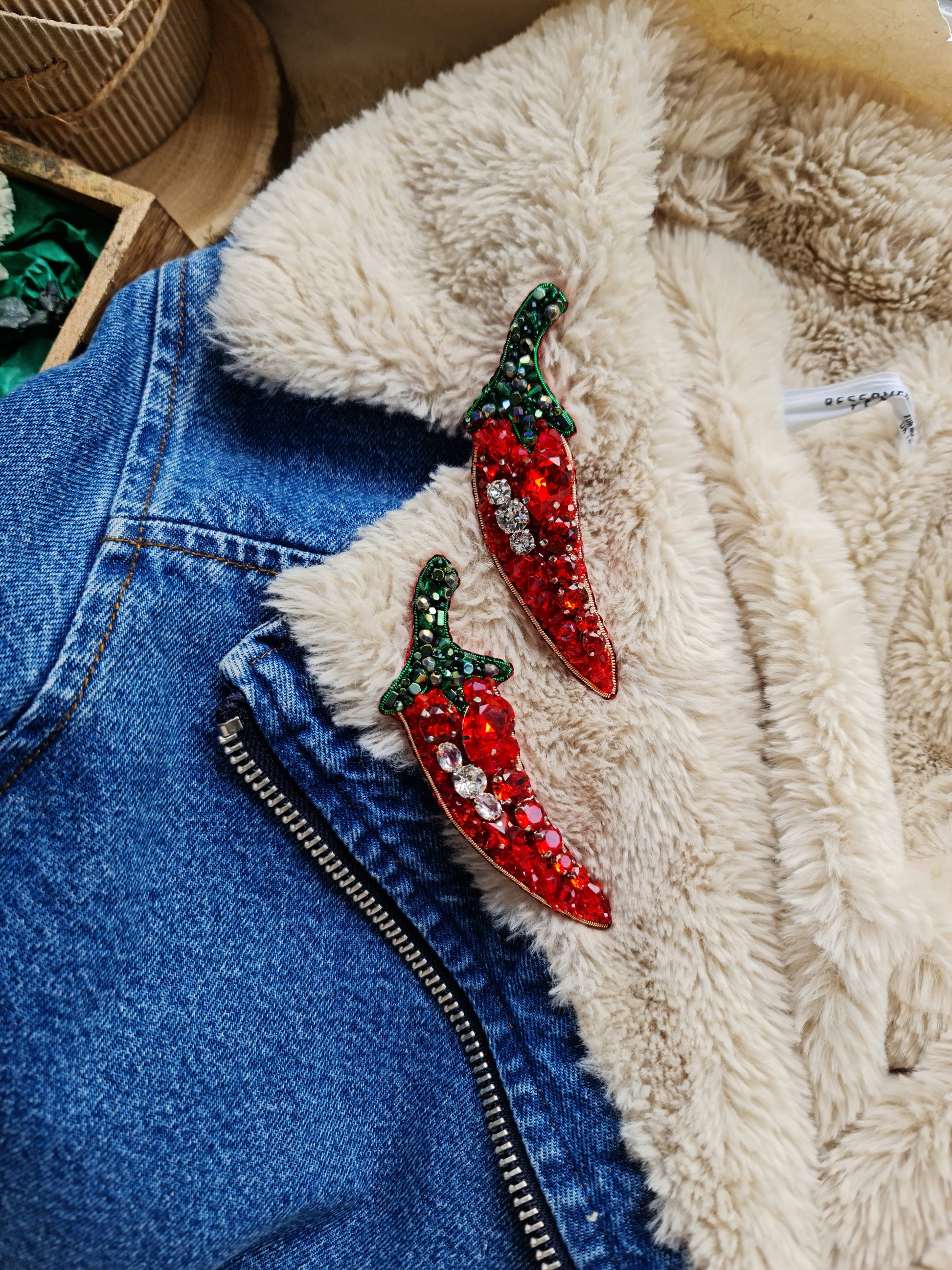 Red chili pepper earrings on a denim jacket with a fluffy beige surface.