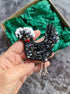 Hand holding a decorative black bird ornament with gemstones against a green textured box.