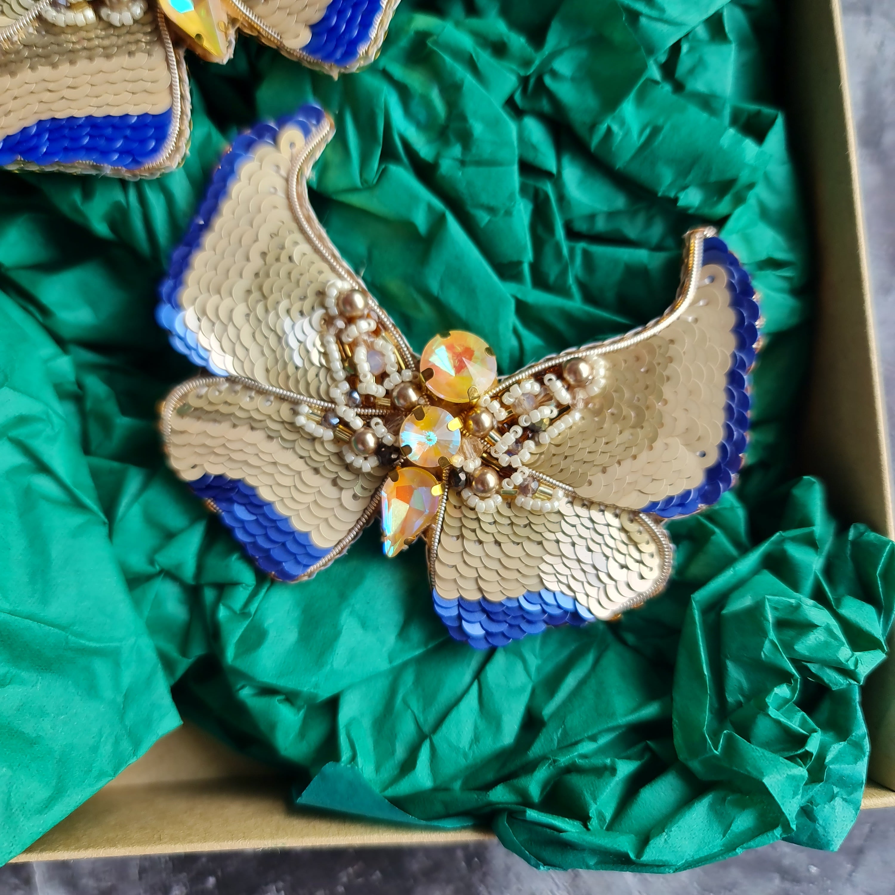 Gold and blue butterfly brooches on green fabric with a dark background