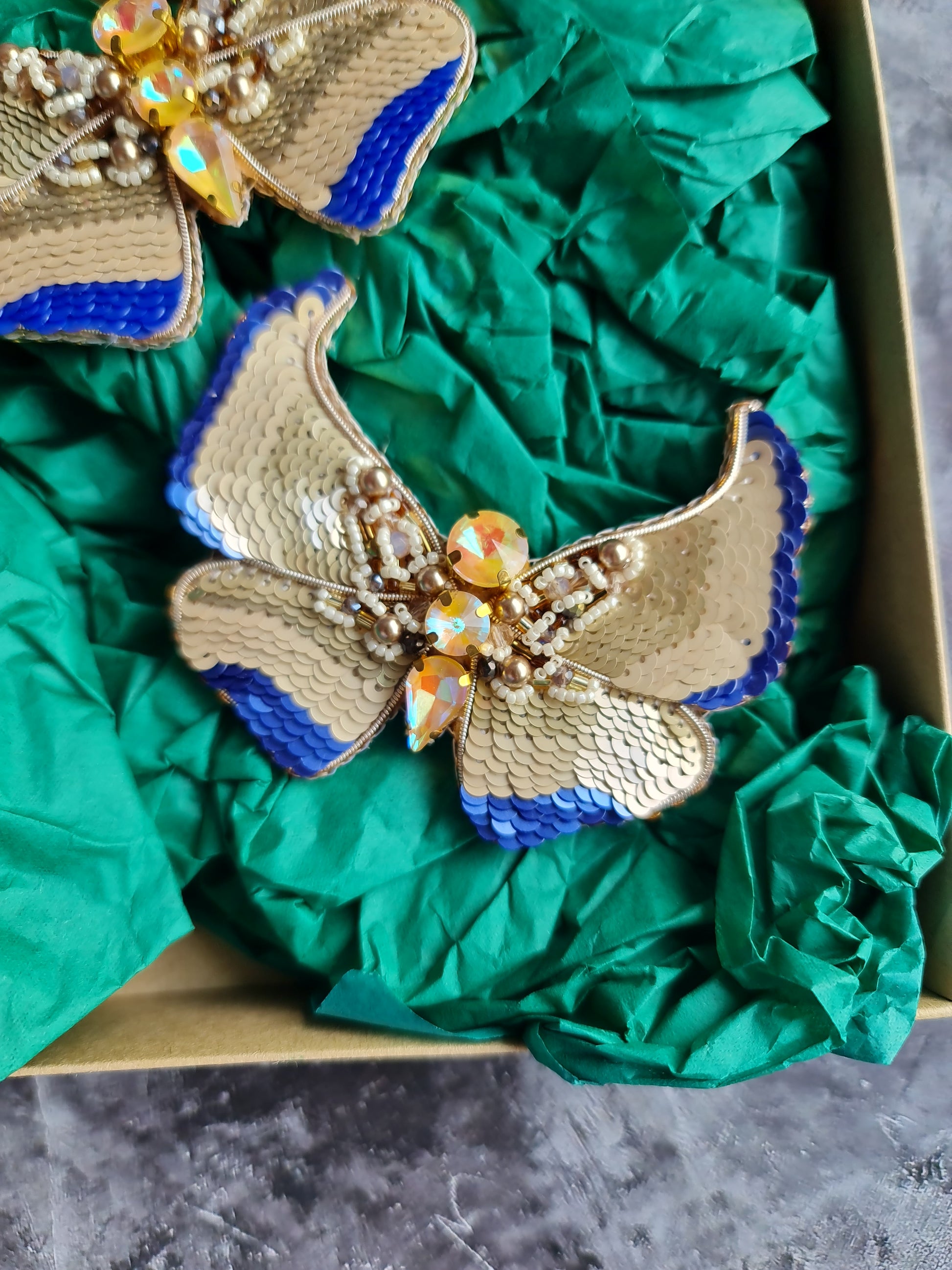 Gold and blue butterfly brooches on green fabric with a dark background