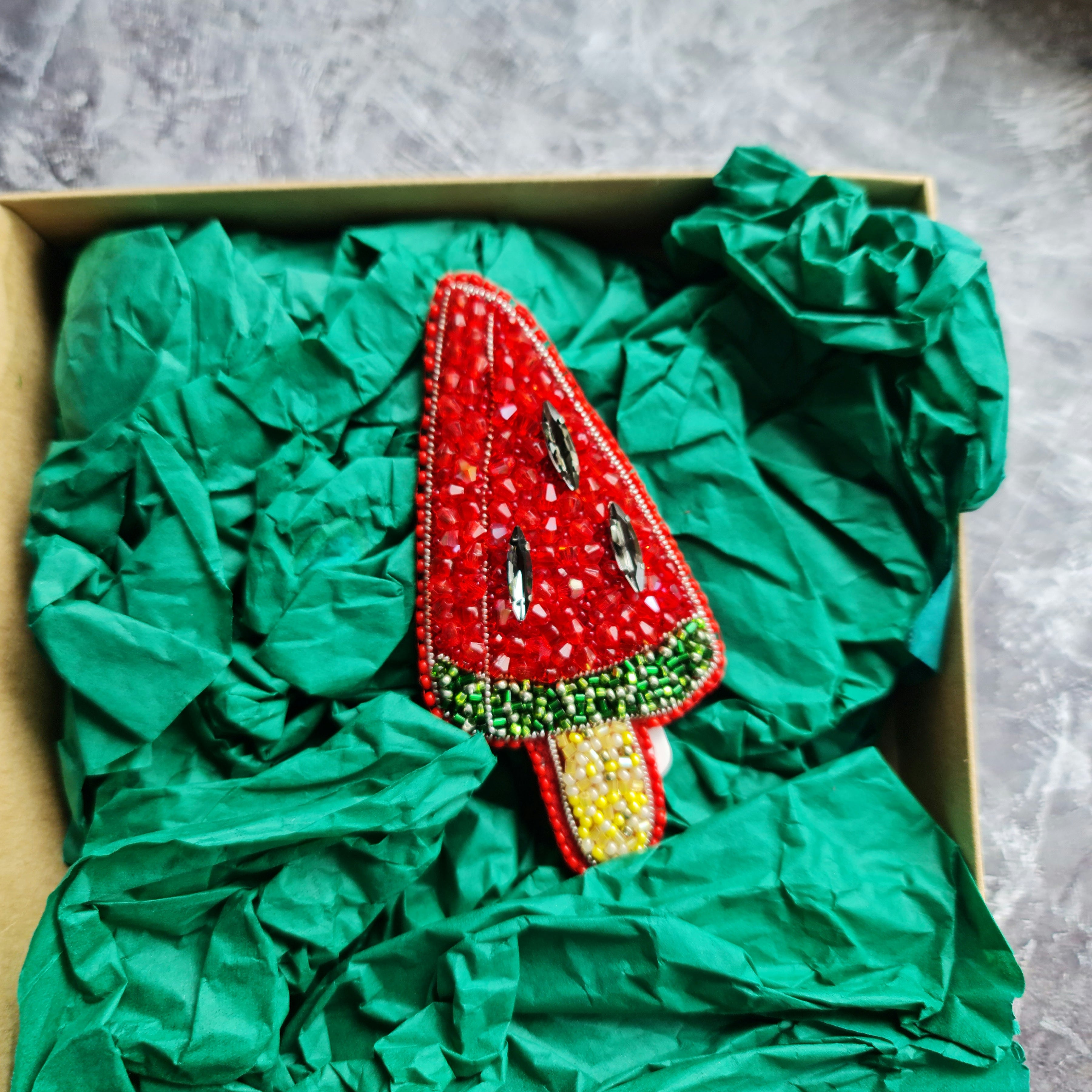Decorative watermelon-shaped item in a box with green tissue paper on a gray surface
