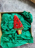 Decorative watermelon-shaped item in a box with green tissue paper on a gray surface