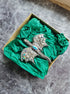 Decorative dragon-shaped brooch in a box with green tissue paper on a gray surface