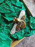 Decorative bee-shaped brooch with gold and silver details on green tissue paper.