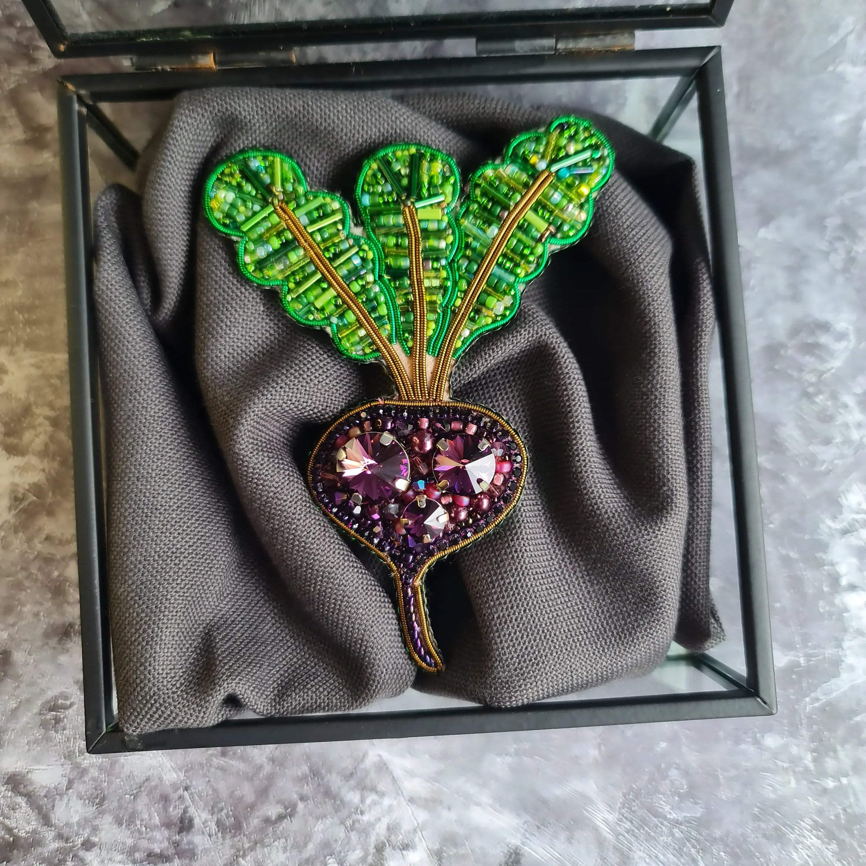 Decorative brooch with gemstones in a glass box on a textured surface