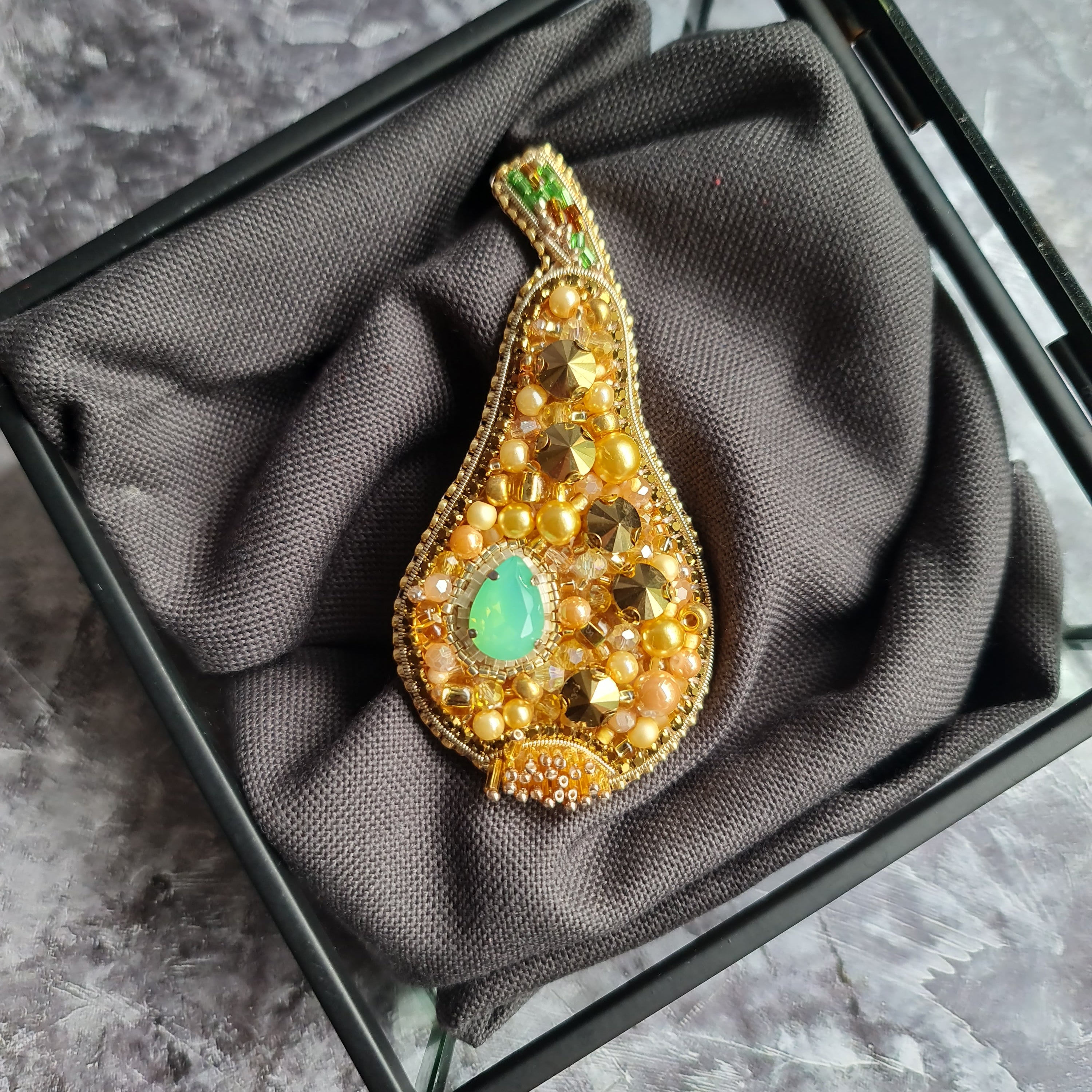 Decorative brooch with gold and green gemstones on a gray fabric background