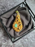 Decorative brooch with gold and green gemstones on a gray fabric background