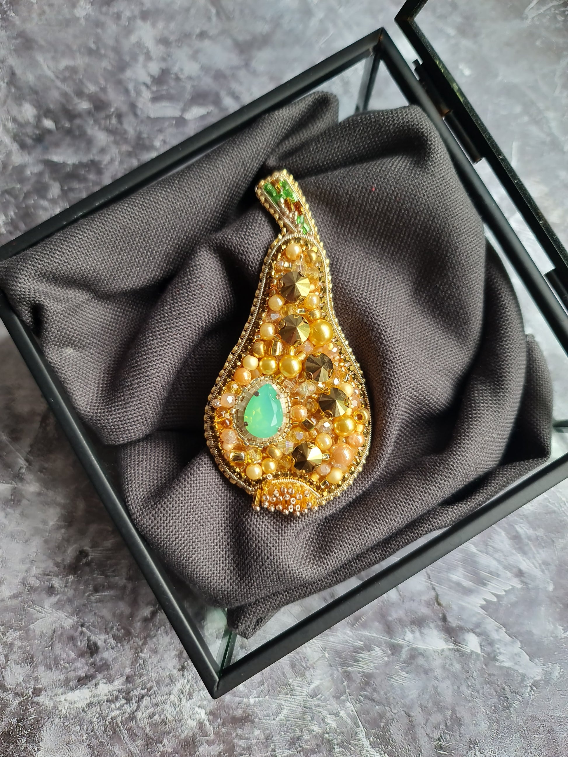 Decorative brooch with gold and green gemstones on a gray fabric background