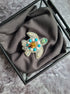Decorative turtle-shaped object with gemstones on a gray fabric inside a glass box.