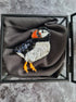 Penguin-shaped brooch in a glass display box on a textured gray surface