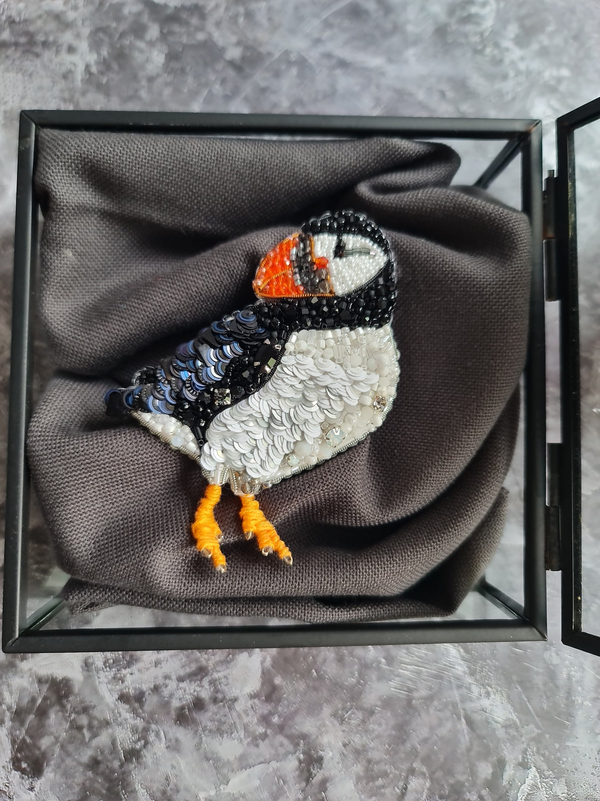 Penguin-shaped brooch in a glass display box on a textured gray surface